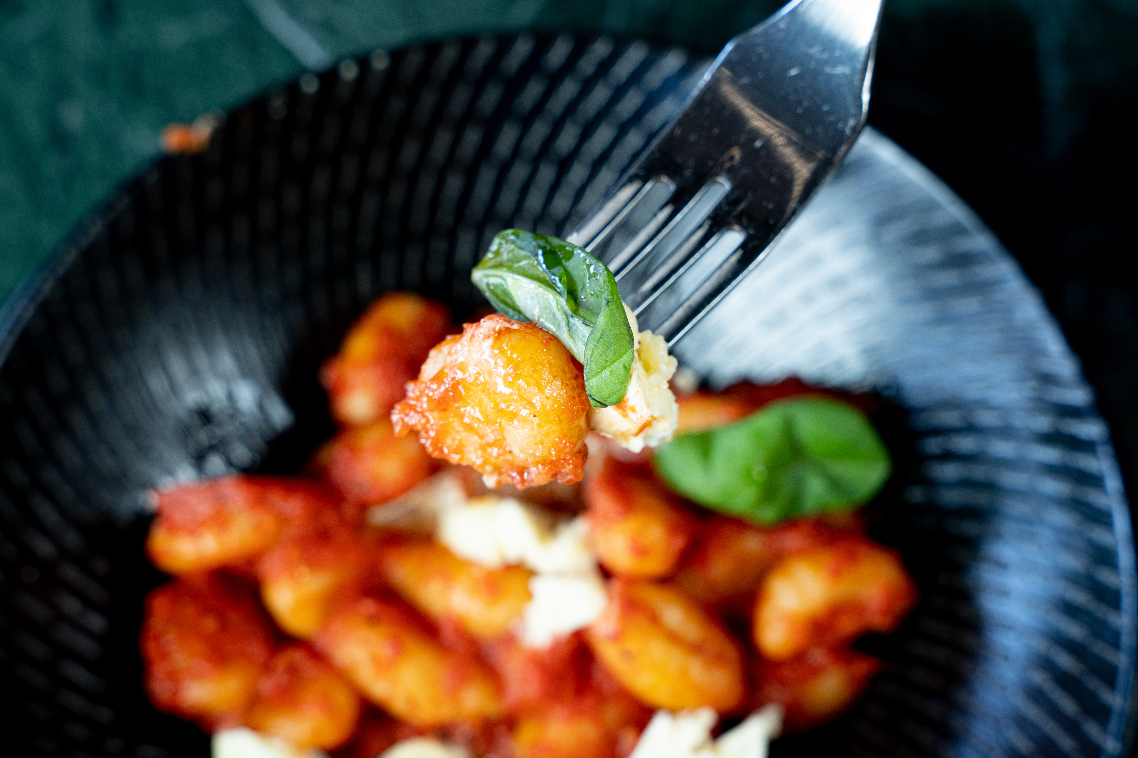 Fork lifting gnocchi in tomato sauce from a black bowl