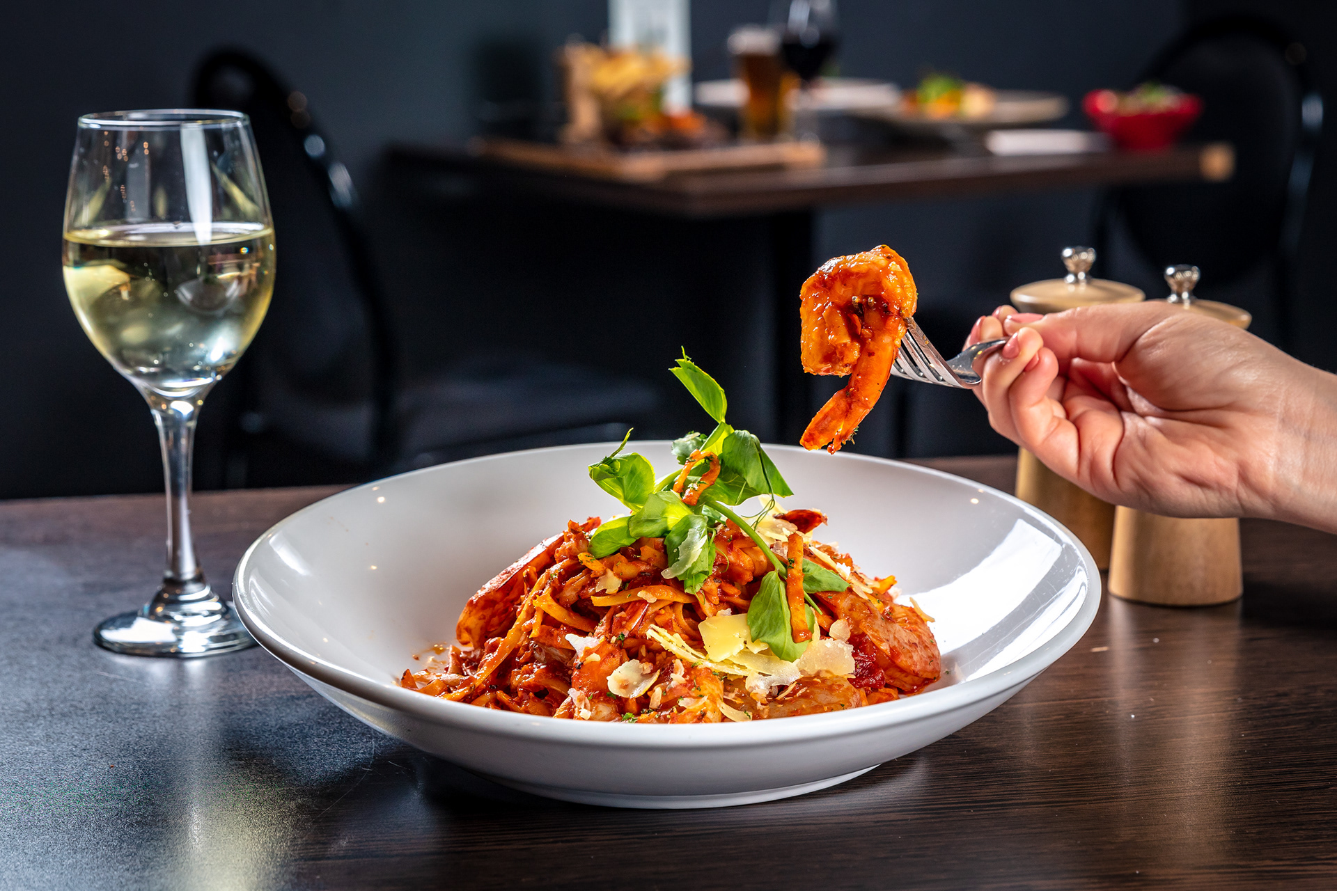 Hands serving a plated restaurant dish beside a wine glass