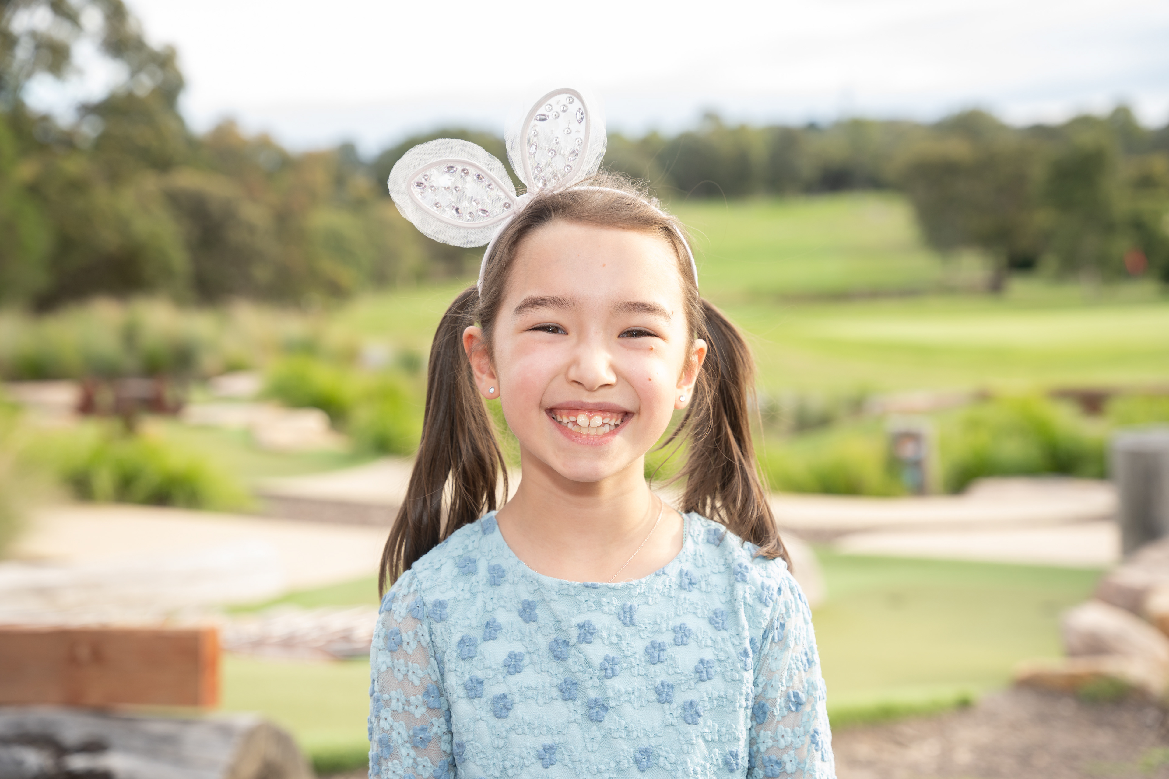 Child smiling in a garden while wearing bunny ears