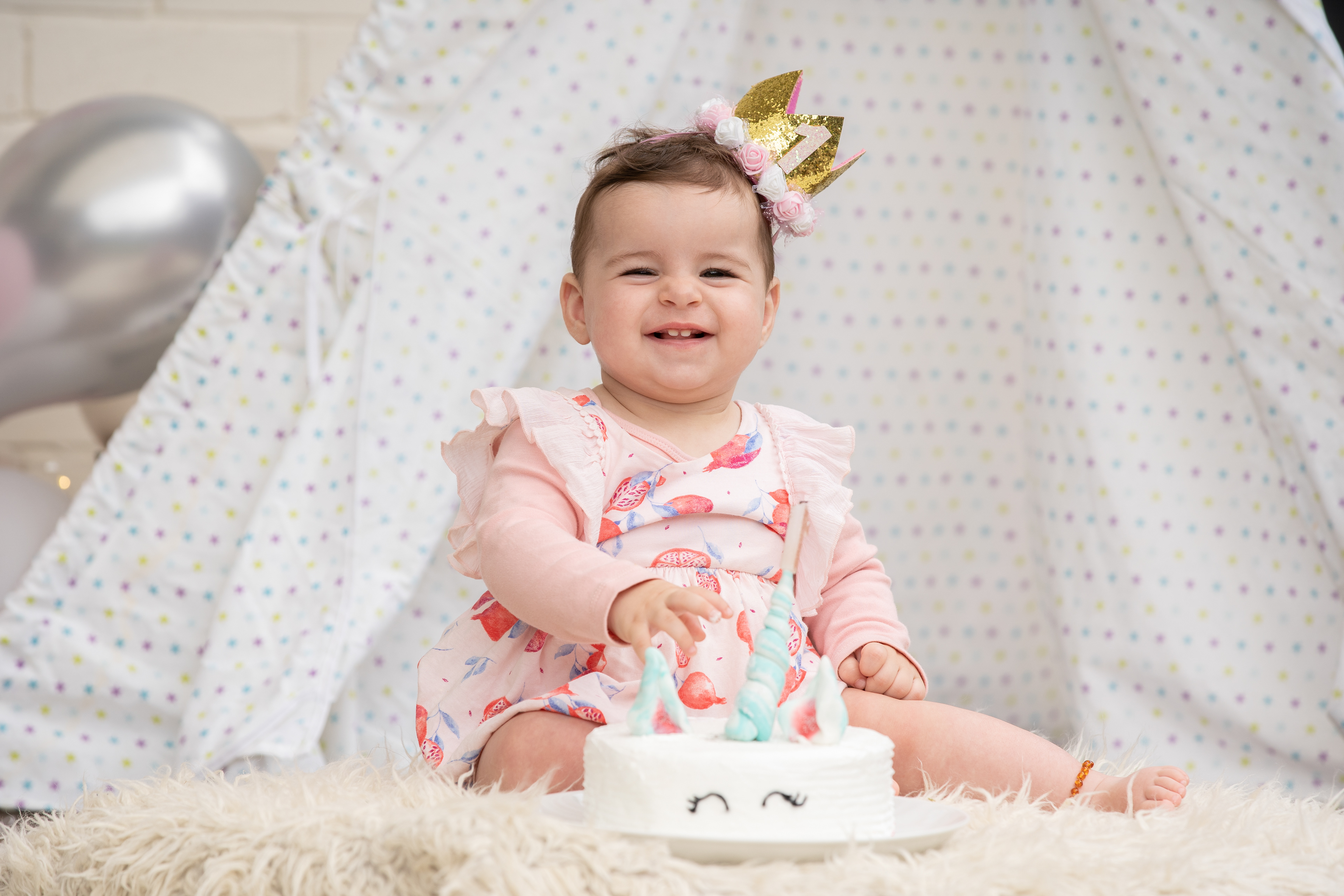 Baby wearing a small crown beside a birthday cake