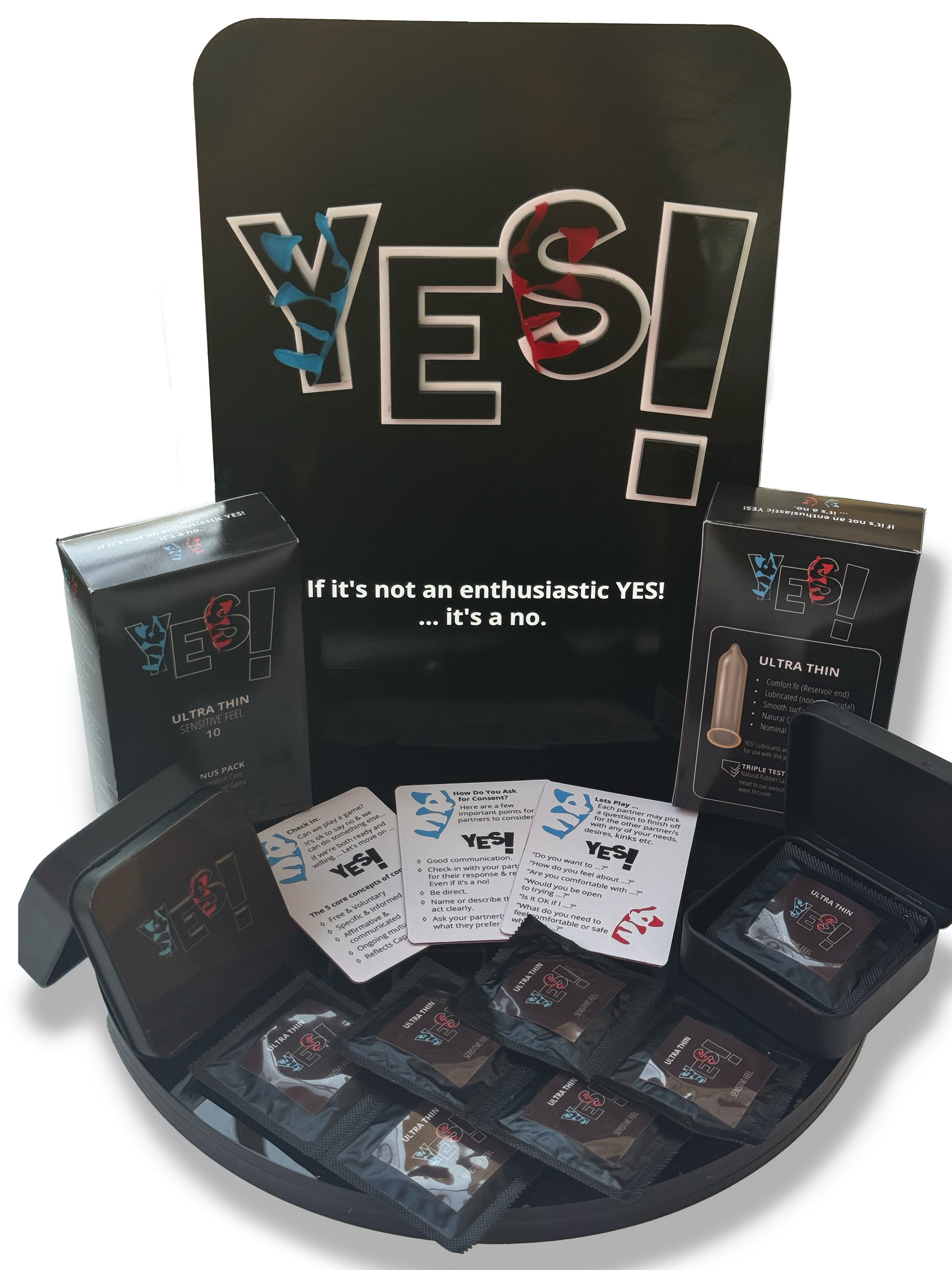 A photograph of a branding concept display for a condom brand that promotes safe sex practices and enthusiastic consent. Featured is a backlit Point of Sale display with the logo and byline 'If it's not an enthusiastic YES! ... It's a NO!', alongside condom packaging, a condom box showing front and back designs, a tin case for carrying condoms, and the playing cards