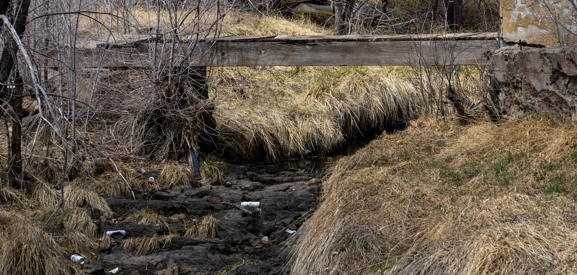 Run down wood bridge above stream filled with trash. 
