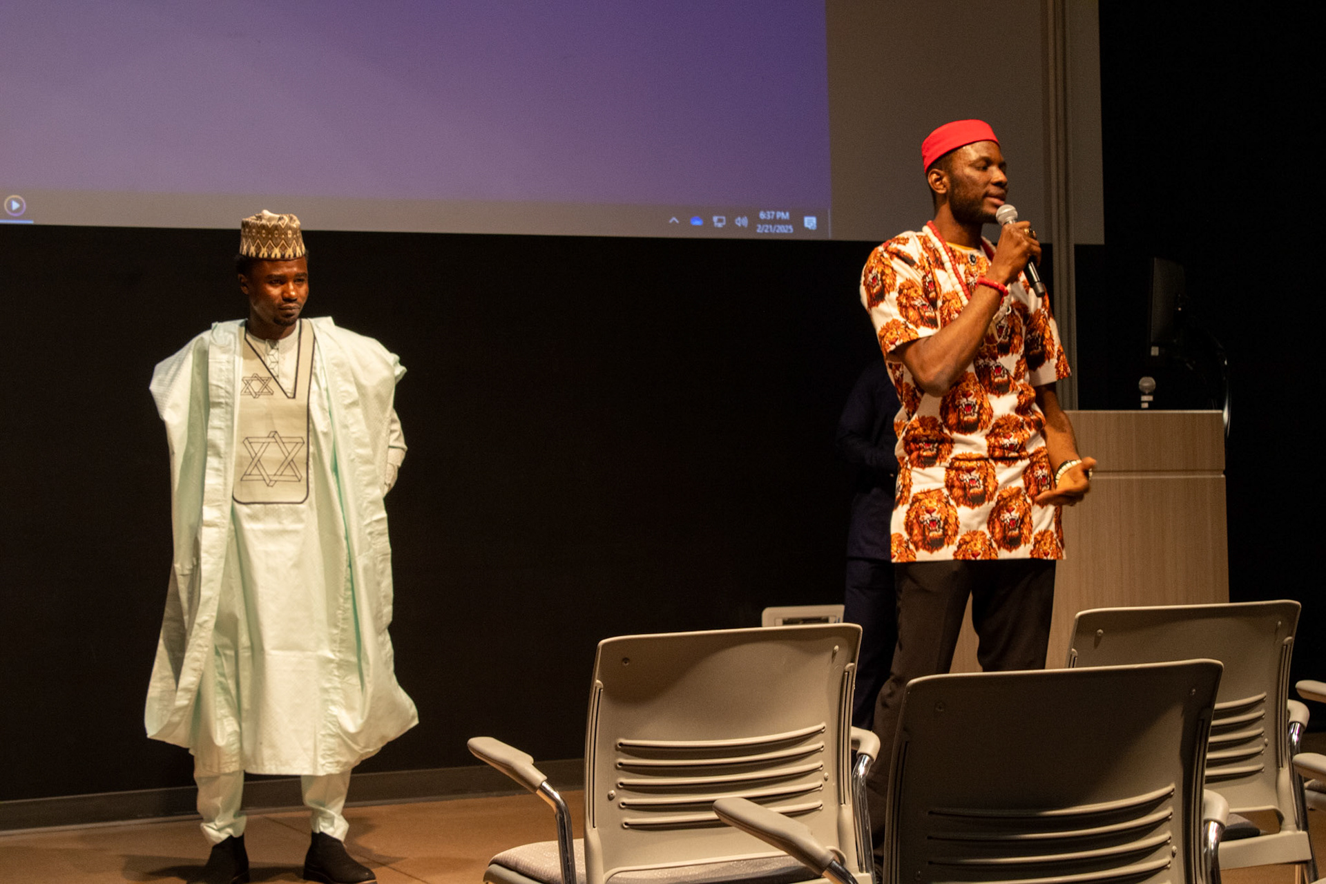Two men standing in front of an audience at the International Pavilion. 