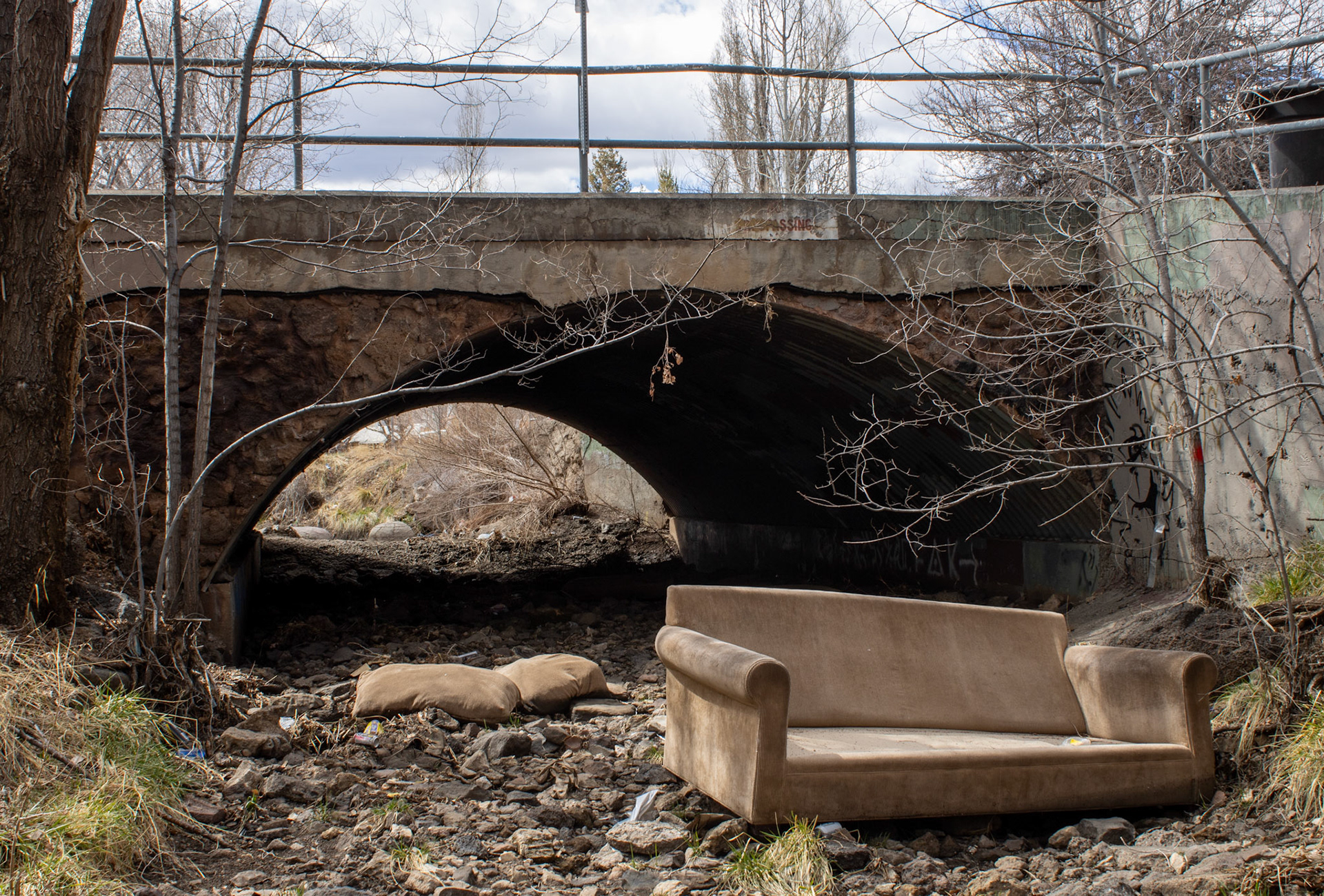 Couch abandoned under bridge in empty stream. 