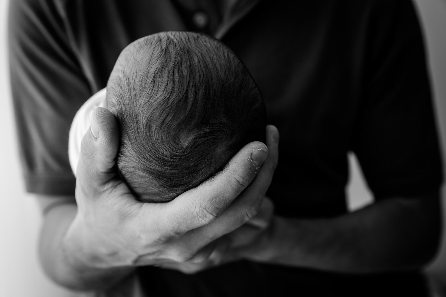 Dad holding newborn head in his hands with side lighting converted to black and white during studio photo session in Manhattan, Kansas by Amy Meng Photography