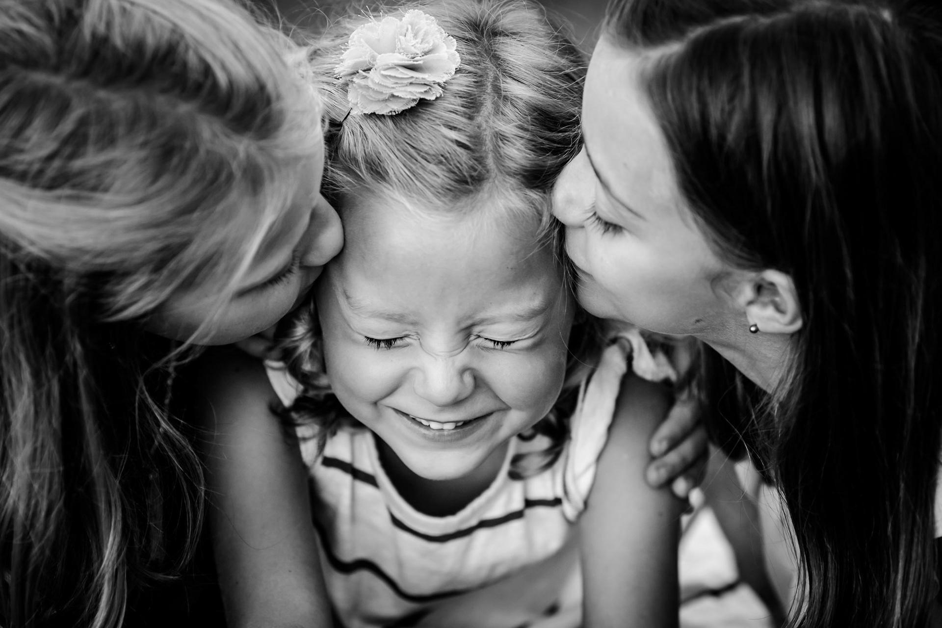 Three sisters. Outer sisters kissing middle sister who is closing eyes and smiling in Manhattan, Kansas by Amy Meng Photography