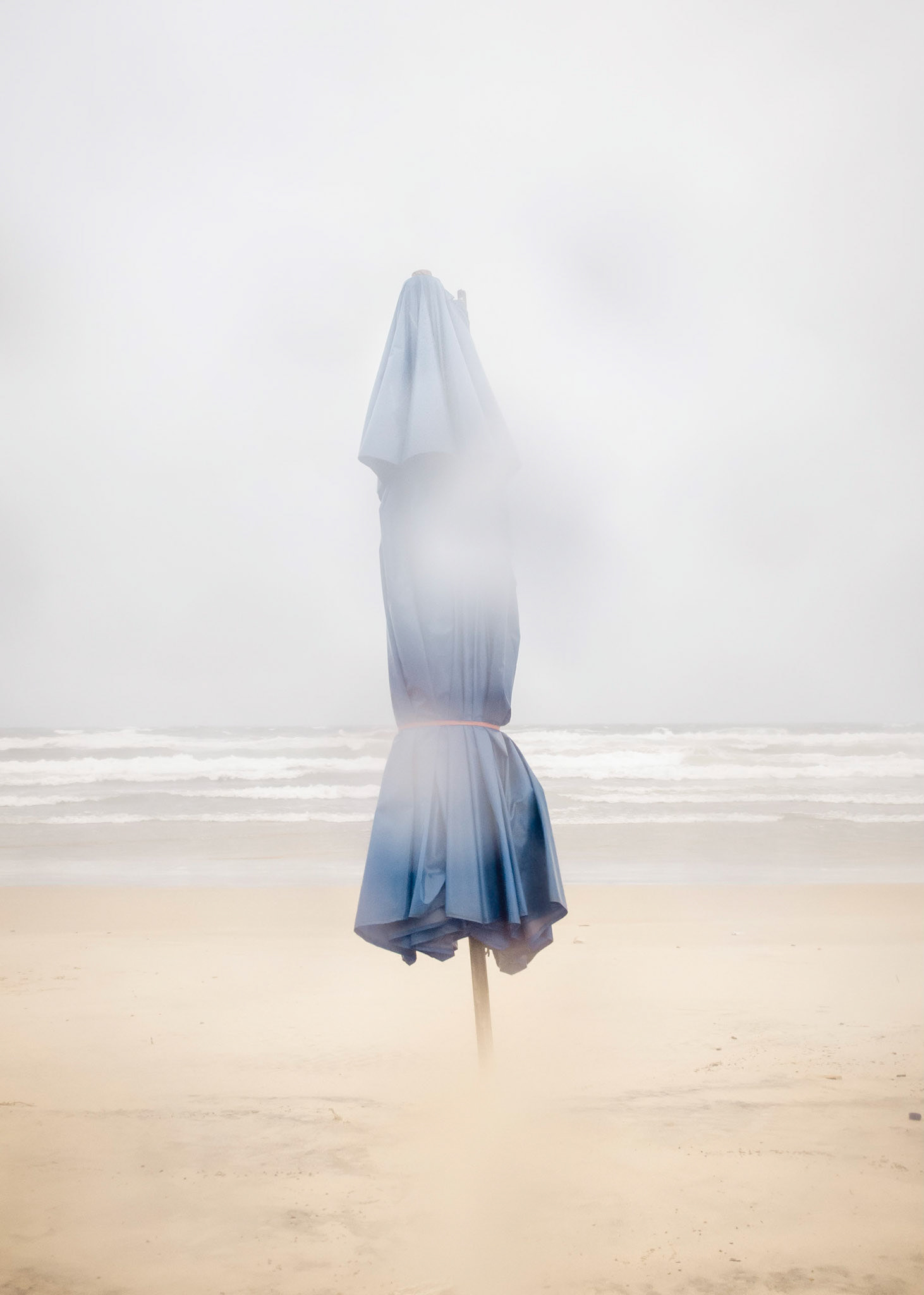 Maria - Our Lady of the Conception, Mother of Heaven and Earth, catholic patroness of Brazil.Janaína - Iemanjá, Mother of Waters, orixá worshiped under the blue mantle of the Virgin Mary in Afro-Brazilian syncretism.Part of Liquid Beach series:As hut owners begun to be expelled from the sands of Salvador’s beaches, their resistance took shape through umbrellas and plastic tables, mythical symbols of the local culture. Their colorful shapes erected against the gloomy horizon set the stage for a visual dictionary of the country's social-economic history, each title referring to an issue yet to be resolved.Liquid - Drinkable amorphous substance. When ingested in despair causes drowning (or drunkenness). Humanity’s current state according to Bauman. Quality of the blood that flows.Beach - Brazilian history’s primordial stage. Where work, leisure and belief mingle. Where blood is boiled, poured and mixed. From where one can see the horizon and feel “saudade”. Where umbrellas arise as sculptures above the sand, watching over the people as saints and orixás.