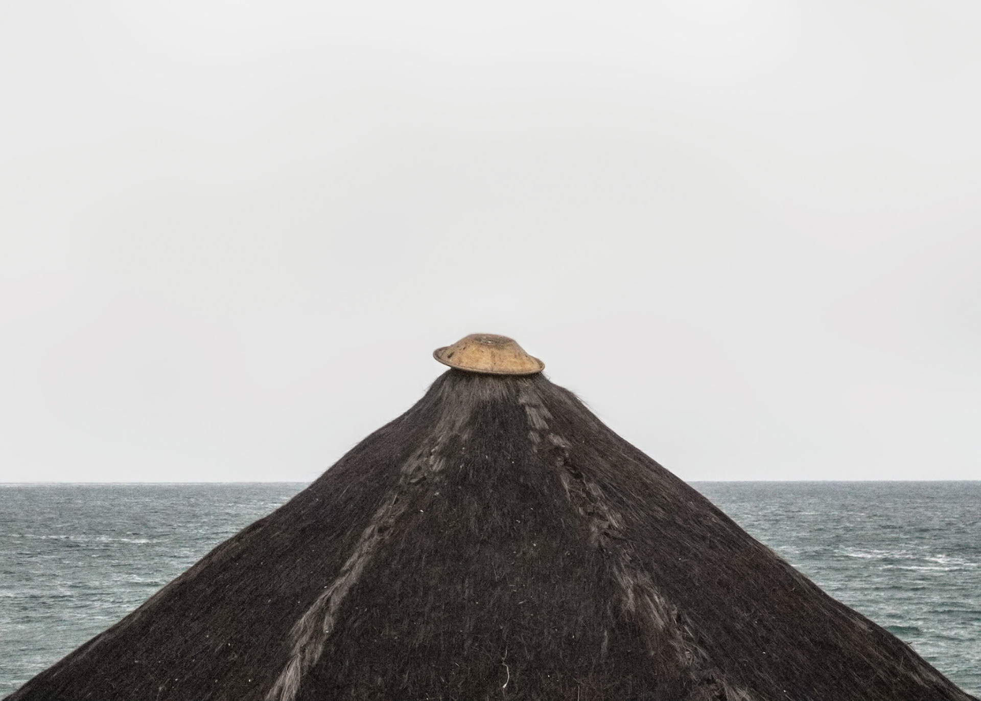 Oca - Tupi word meaning house. Wood construction covered by vegetal fibers used by Brazilian indians as a home for one or more families.Part of Liquid Beach series:As hut owners begun to be expelled from the sands of Salvador’s beaches, their resistance took shape through umbrellas and plastic tables, mythical symbols of the local culture. Their colorful shapes erected against the gloomy horizon set the stage for a visual dictionary of the country's social-economic history, each title referring to an issue yet to be resolved.Liquid - Drinkable amorphous substance. When ingested in despair causes drowning (or drunkenness). Humanity’s current state according to Bauman. Quality of the blood that flows.Beach - Brazilian history’s primordial stage. Where work, leisure and belief mingle. Where blood is boiled, poured and mixed. From where one can see the horizon and feel “saudade”. Where umbrellas arise as sculptures above the sand, watching over the people as saints and orixás.