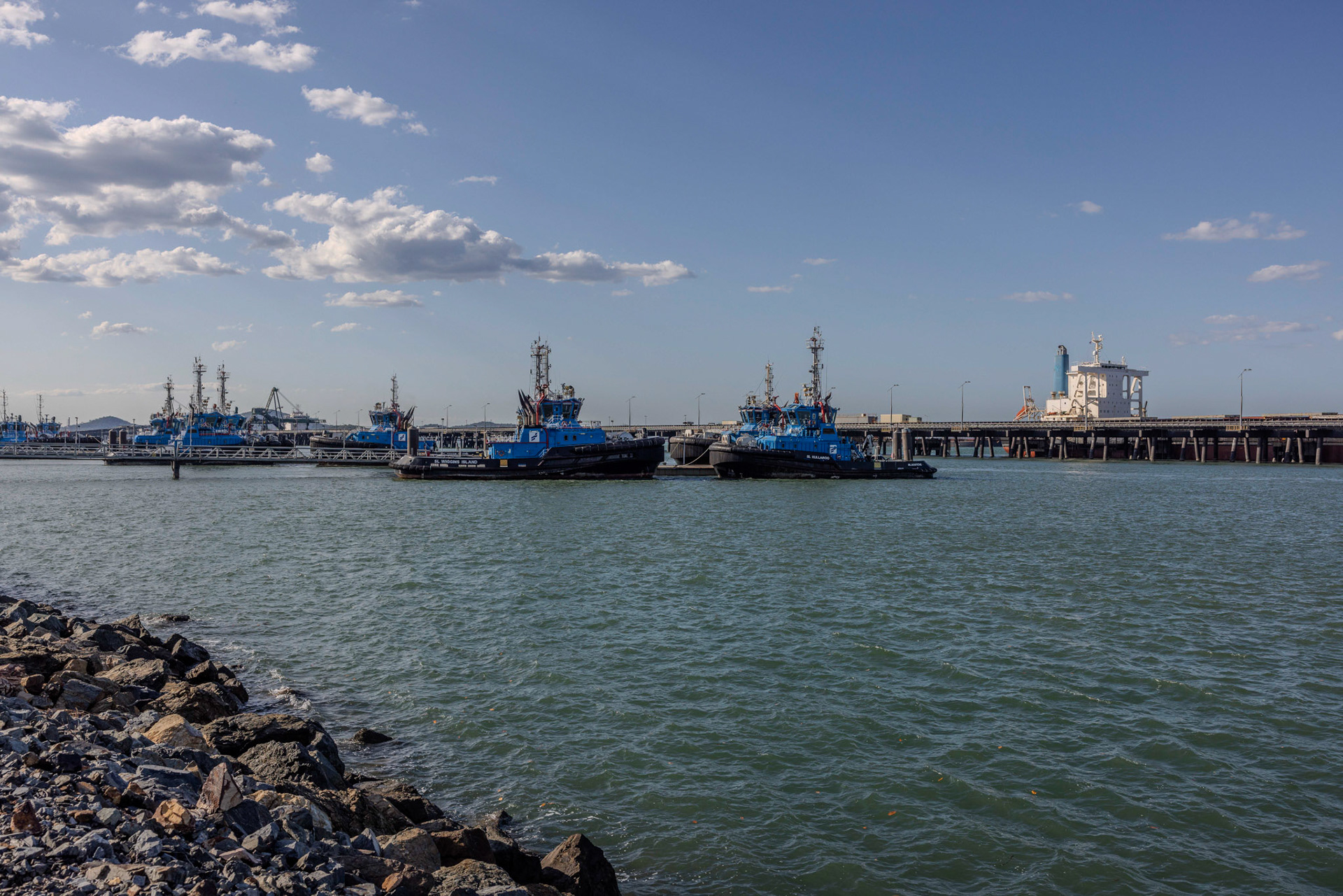 Boats ready for action Port of Gladstone. The vibrant scene at the Port of Gladstone captures a bustling hub of activity, with a fleet of boats docked and ready for action. The port is a critical nexus for both traditional industries and emerging renewable energy projects, supporting local and national economies. The image reflects the region’s adaptability and ambition as it navigates the move to a future of more sustainable energy while continuing to honour its rich maritime heritage.