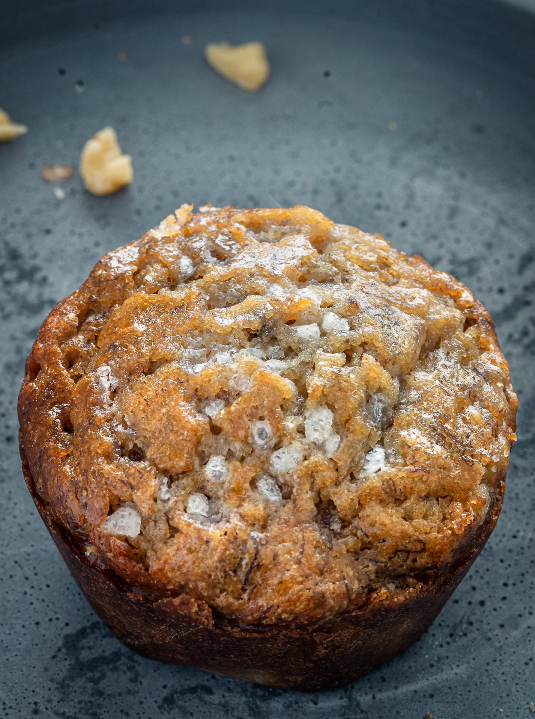 Extreme close-up of the top of a banana walnut muffin highlighting the crunchy sugar topping and toasted walnuts.