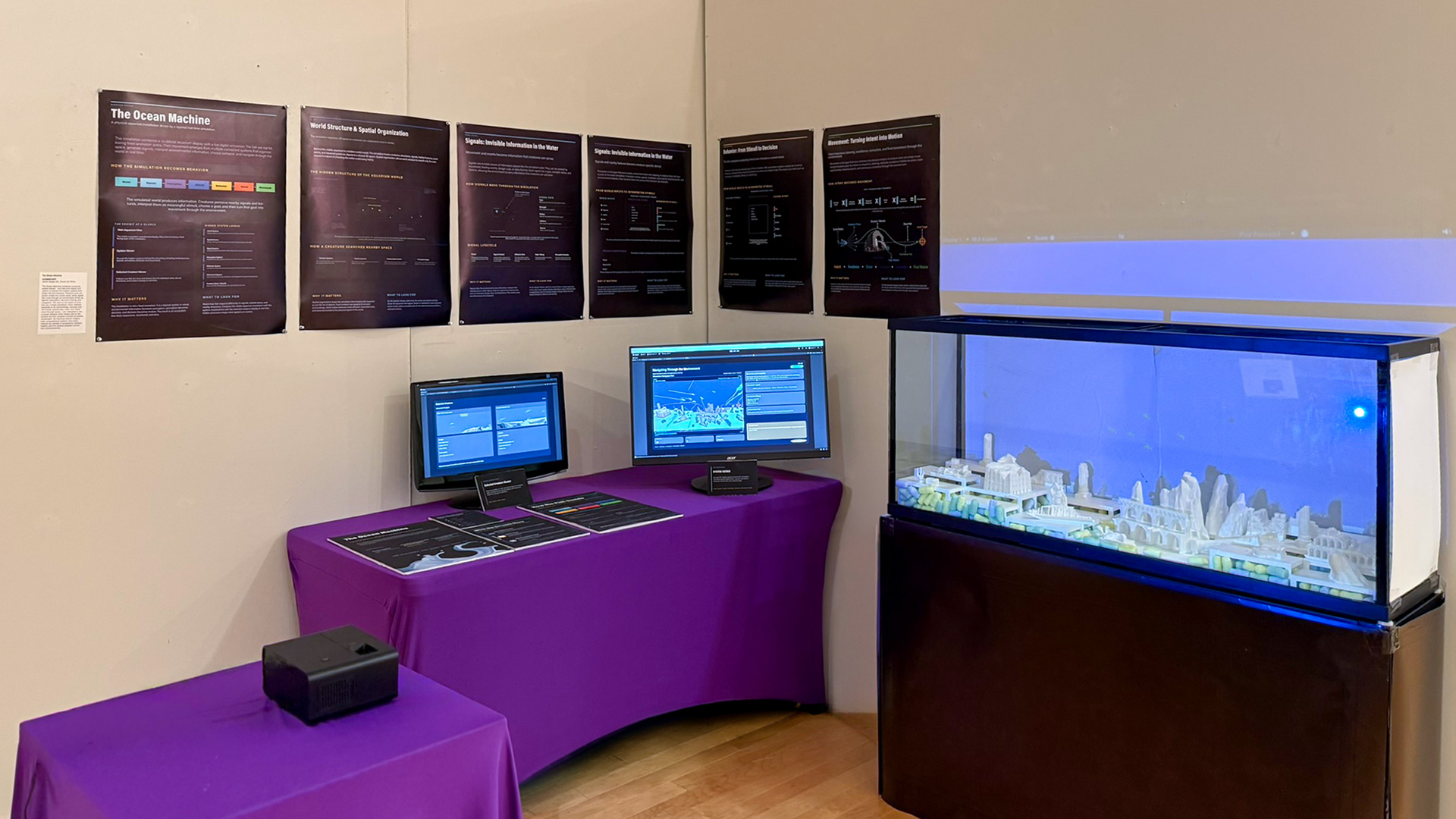 Full installation view — The completed capstone display with physical aquarium, projected simulation, secondary monitors, table graphics, and wall posters.