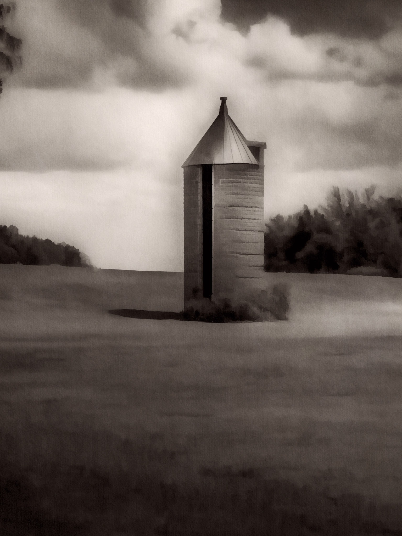 A solitary silo rises from a quiet rural landscape beneath a heavy sky.