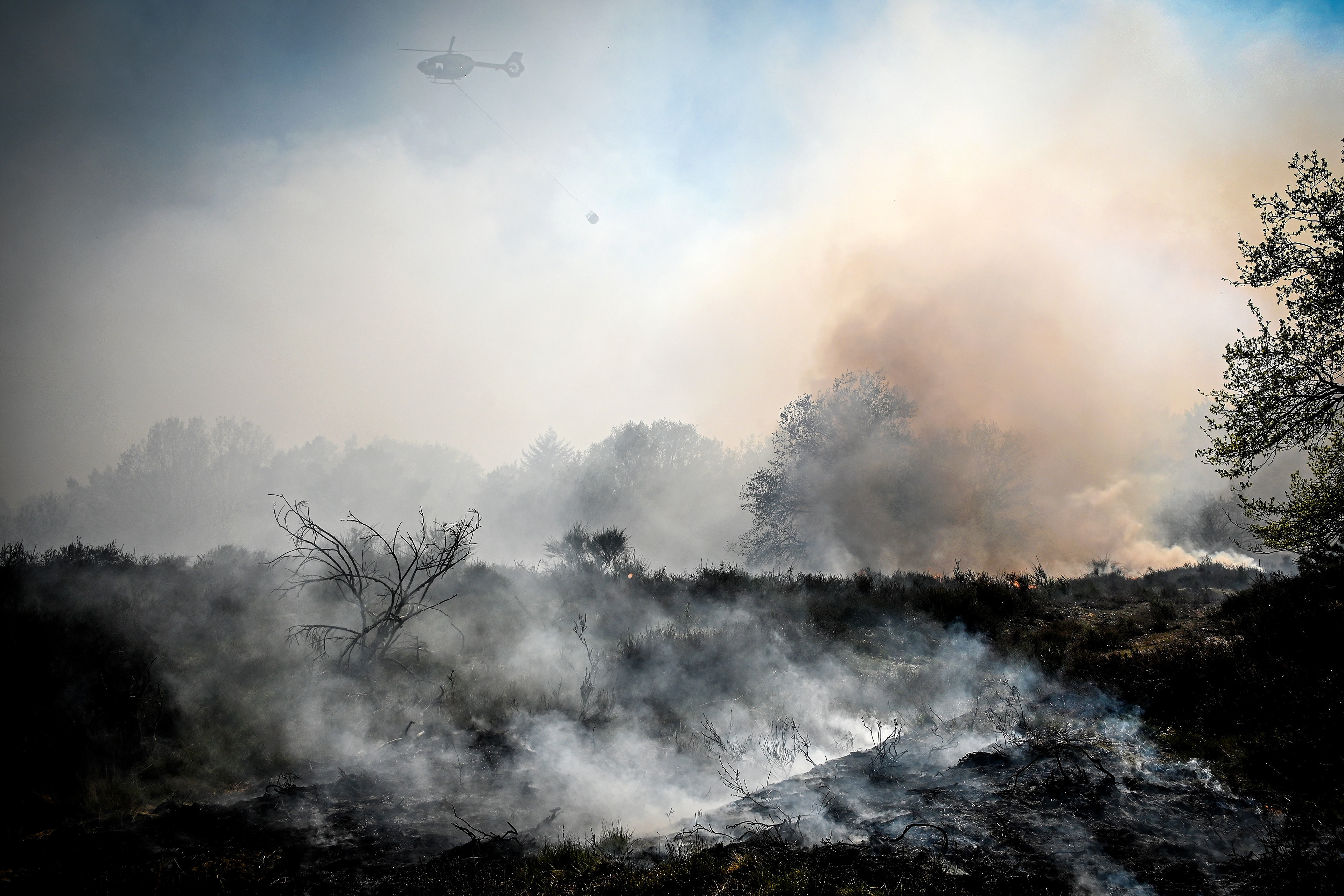 A helicopter throws water over a point of fire during a forest fire at the national park De Meinweg in the German-Dutch border area near Niederkruechten, Germany, 21 April 2020. (Photo by Sascha Steinbach/epa)