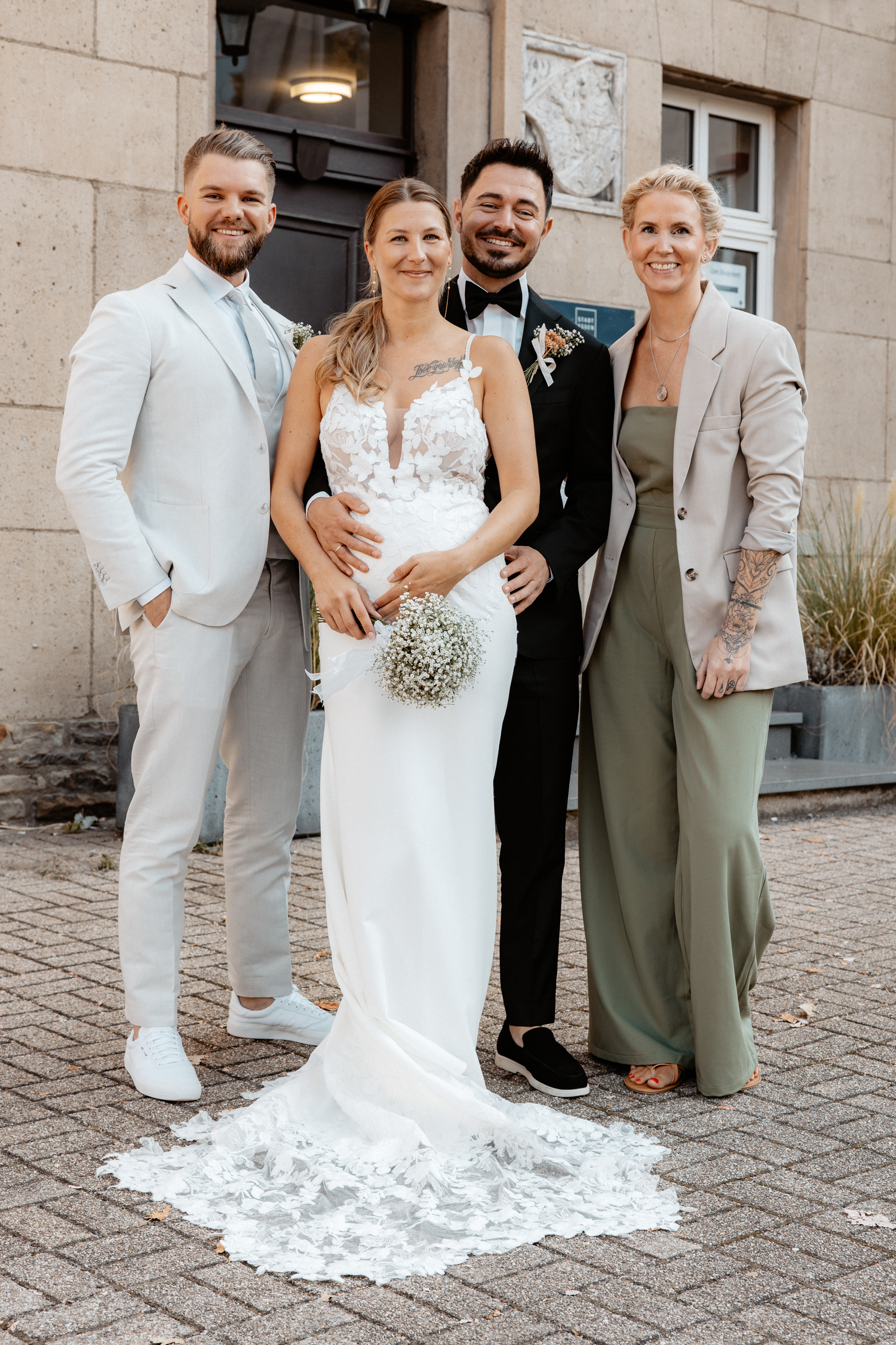 Justine und Maurice posieren mit ihren Trauzeugen für ein Hochzeitsfoto vor dem Rathaus in Essen-Kettwig.