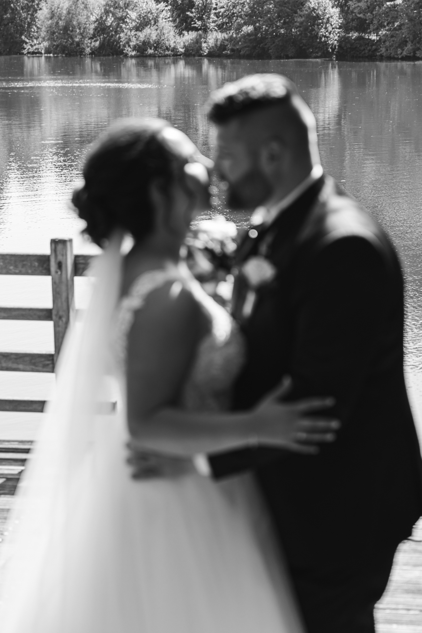 Schwarz-Weiß-Fotografie des Brautpaares vor einem See – eine kunstvolle Aufnahme mit romantischer Unschärfe.