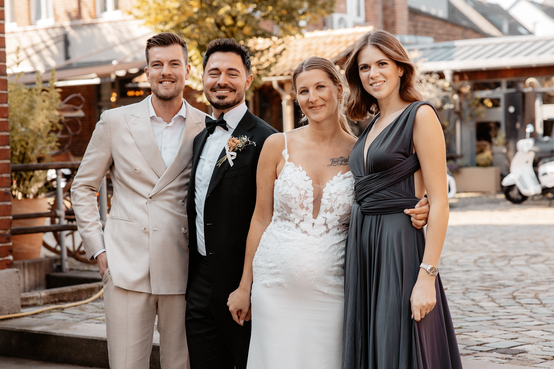 Das Brautpaar posiert für ein Gruppenfoto mit zwei engen Freunden, beide Paare strahlen glücklich in die Kamera.