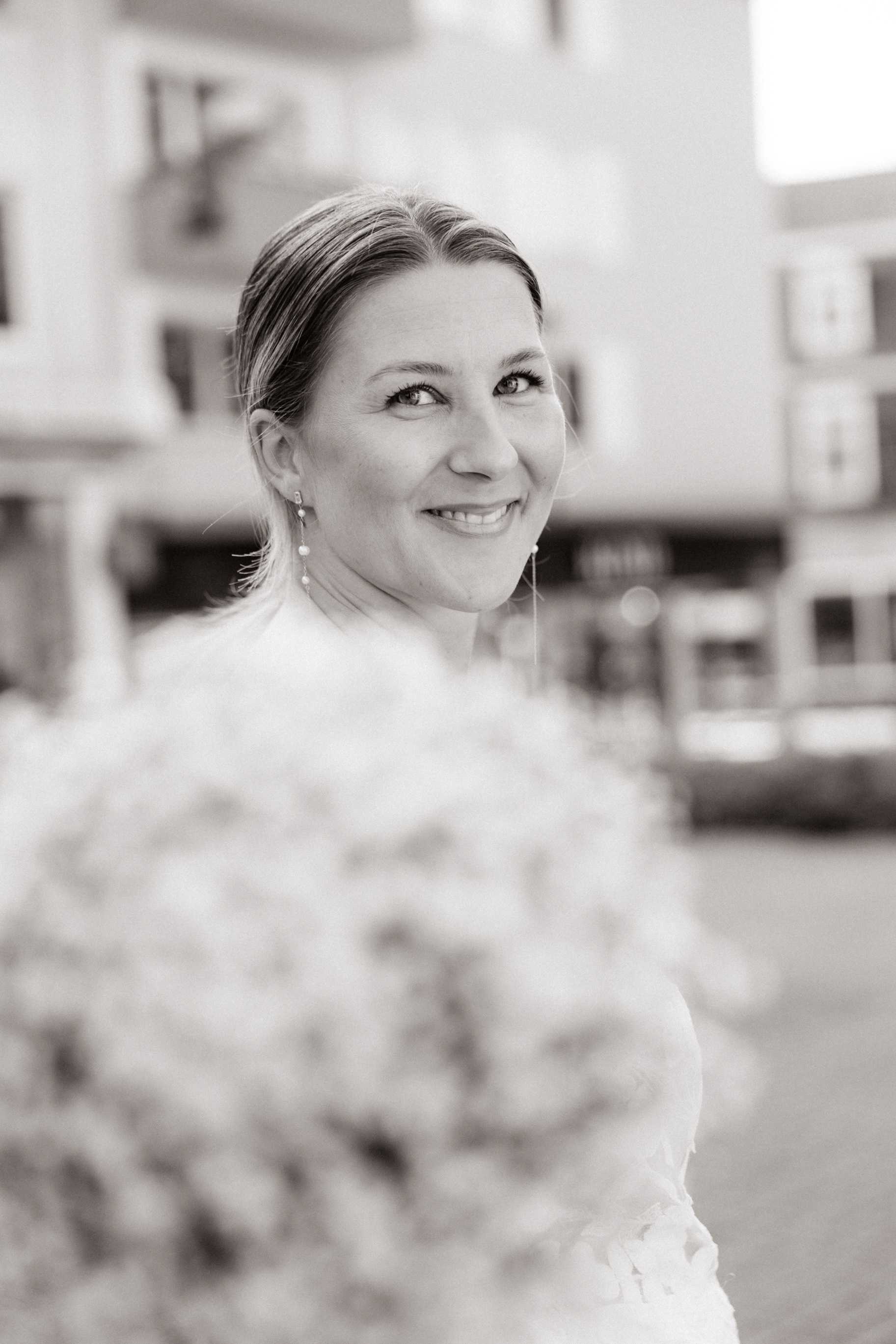Stilvolles Schwarz-Weiß-Porträt der Braut mit einem sanften Lächeln, während ihr Brautstrauß den Vordergrund verschwimmen lässt.