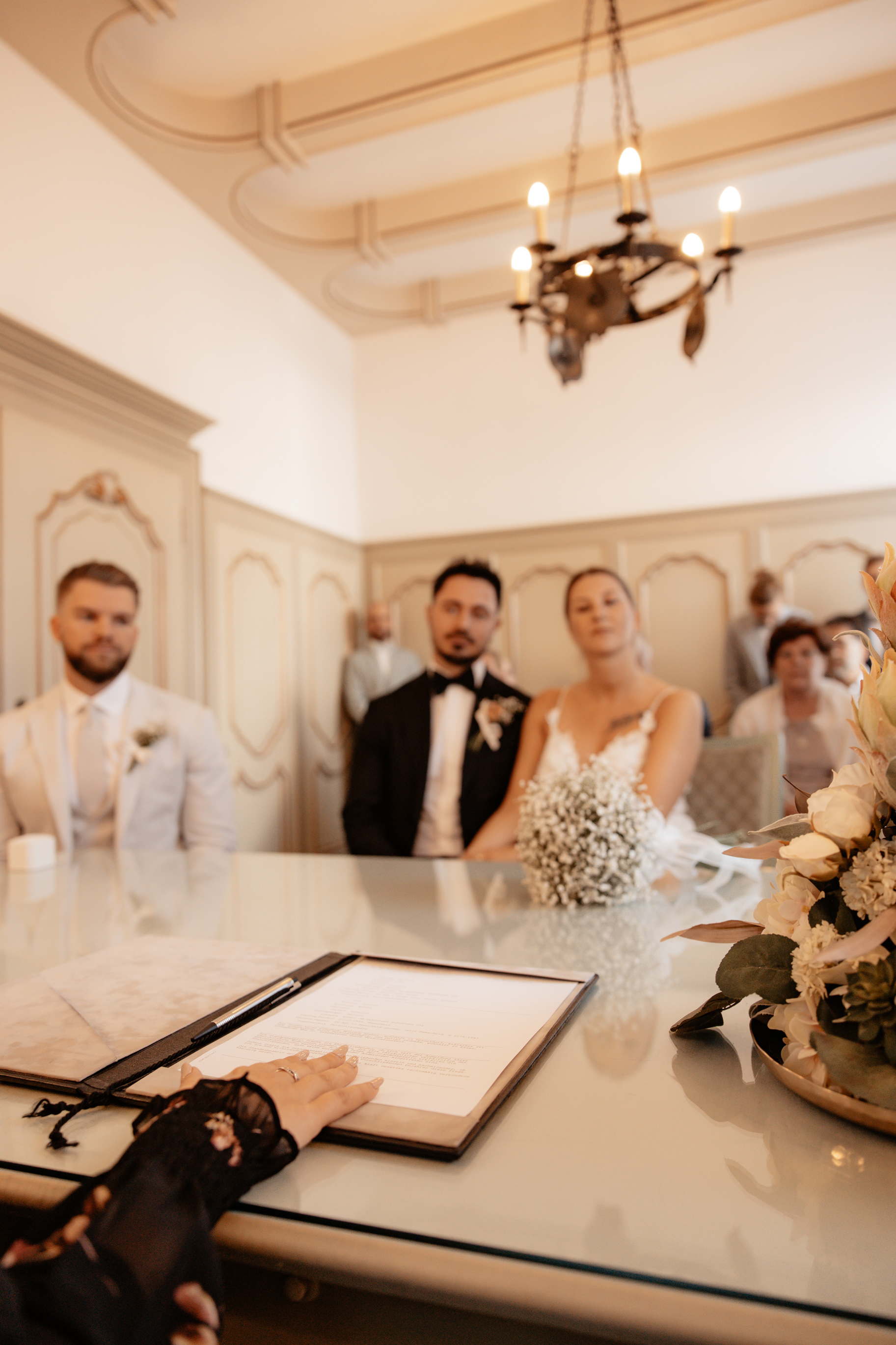 Zeremonie aus der Perspektive der Standesbeamtin – das Brautpaar konzentriert sich auf die Eheschließung, während Gäste im Hintergrund die emotionale Szene verfolgen.
