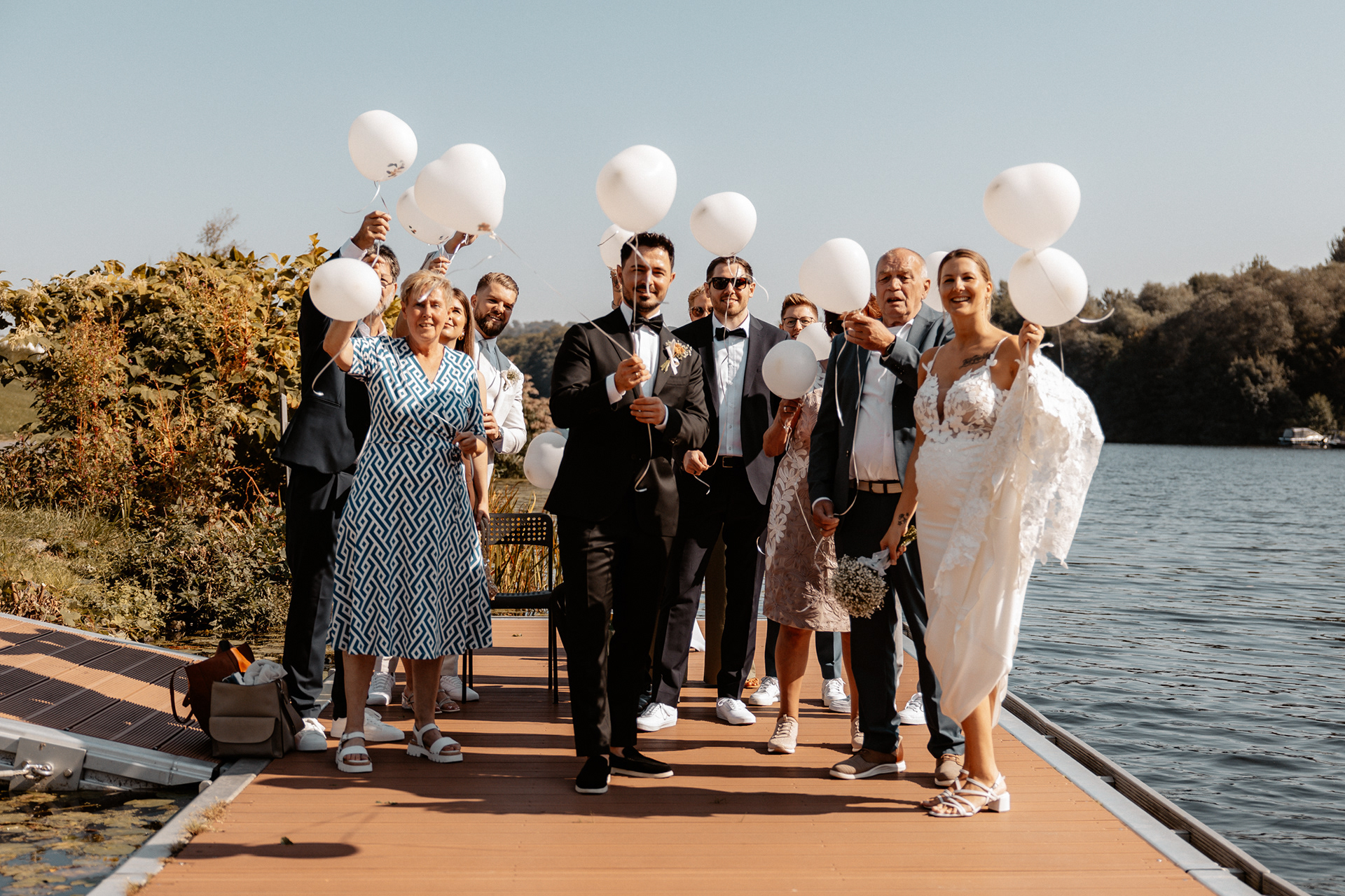 Die Hochzeitsgesellschaft versammelt sich auf dem Steg am Wasser, bereit, weiße Luftballons in den Himmel steigen zu lassen.