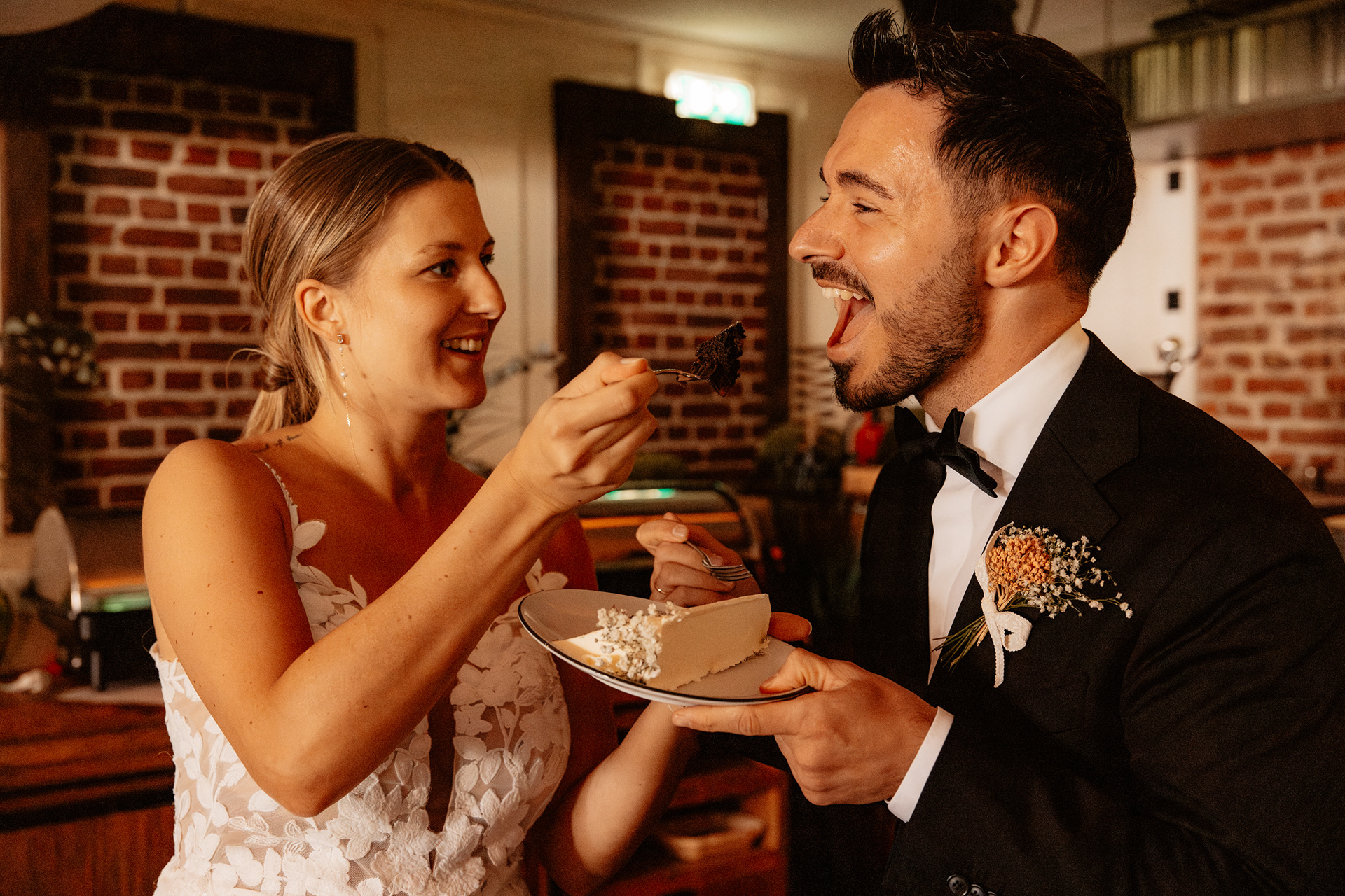 Die Braut füttert den Bräutigam spielerisch mit einem Stück Hochzeitstorte, während er lachend den Mund öffnet