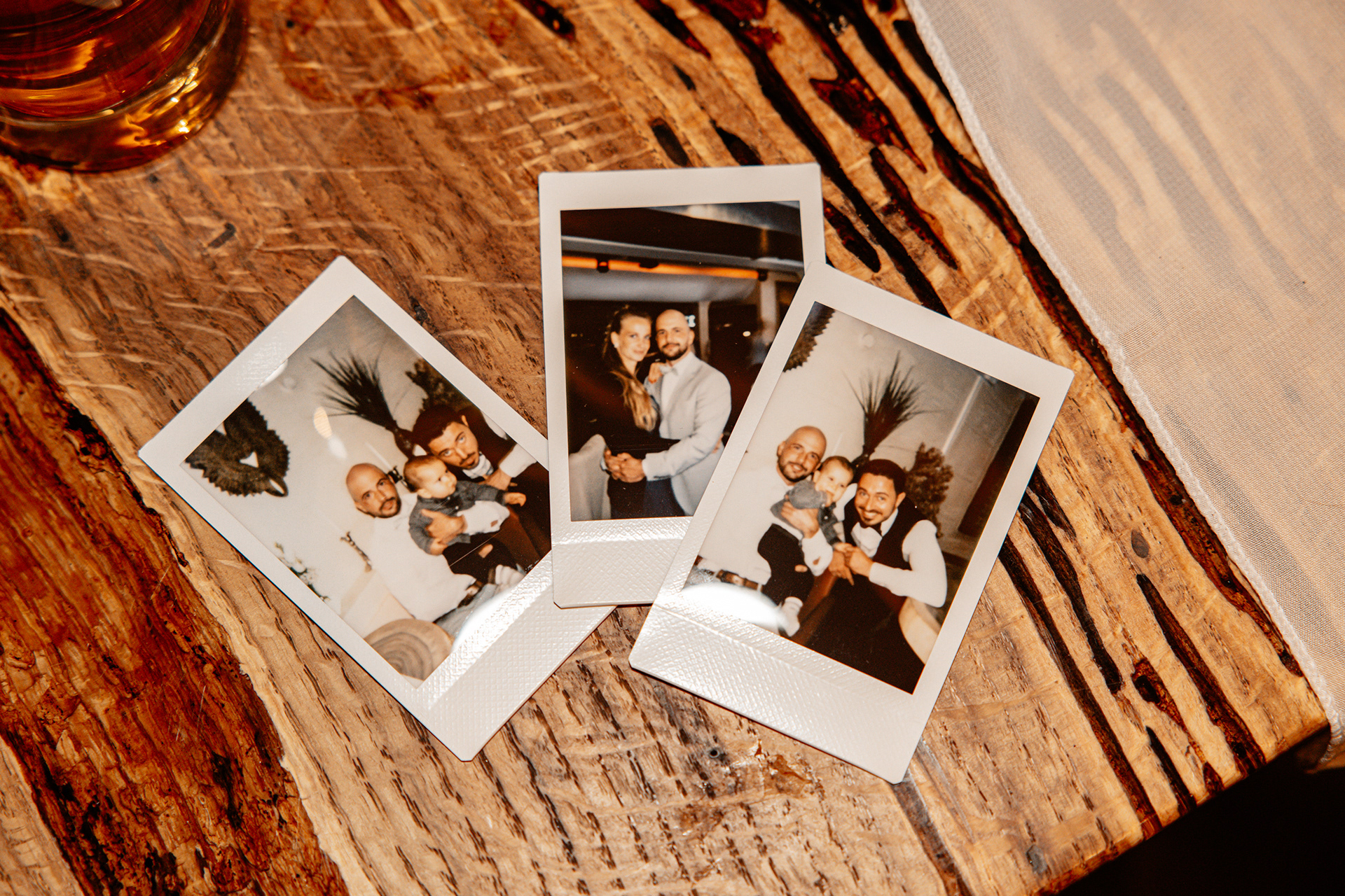 Drei Polaroid-Fotos liegen auf einem rustikalen Holztisch, die Erinnerungen an besondere Hochzeitsmomente mit Familie und Freunden festhalten.