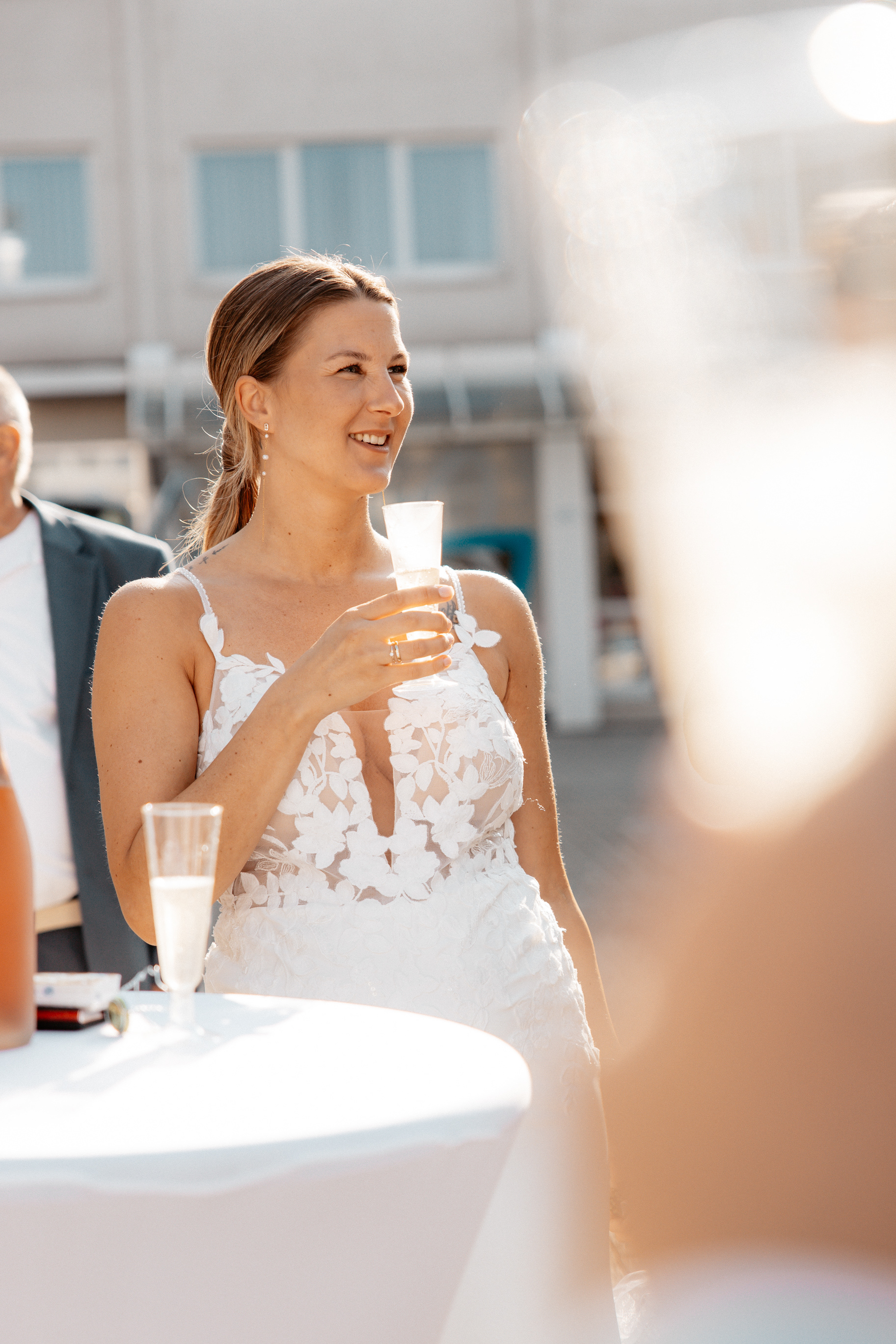 Die strahlende Braut Justine hält ein alkoholfreies Sektglas in der Hand und genießt den Hochzeitsmoment im Sonnenschein.
