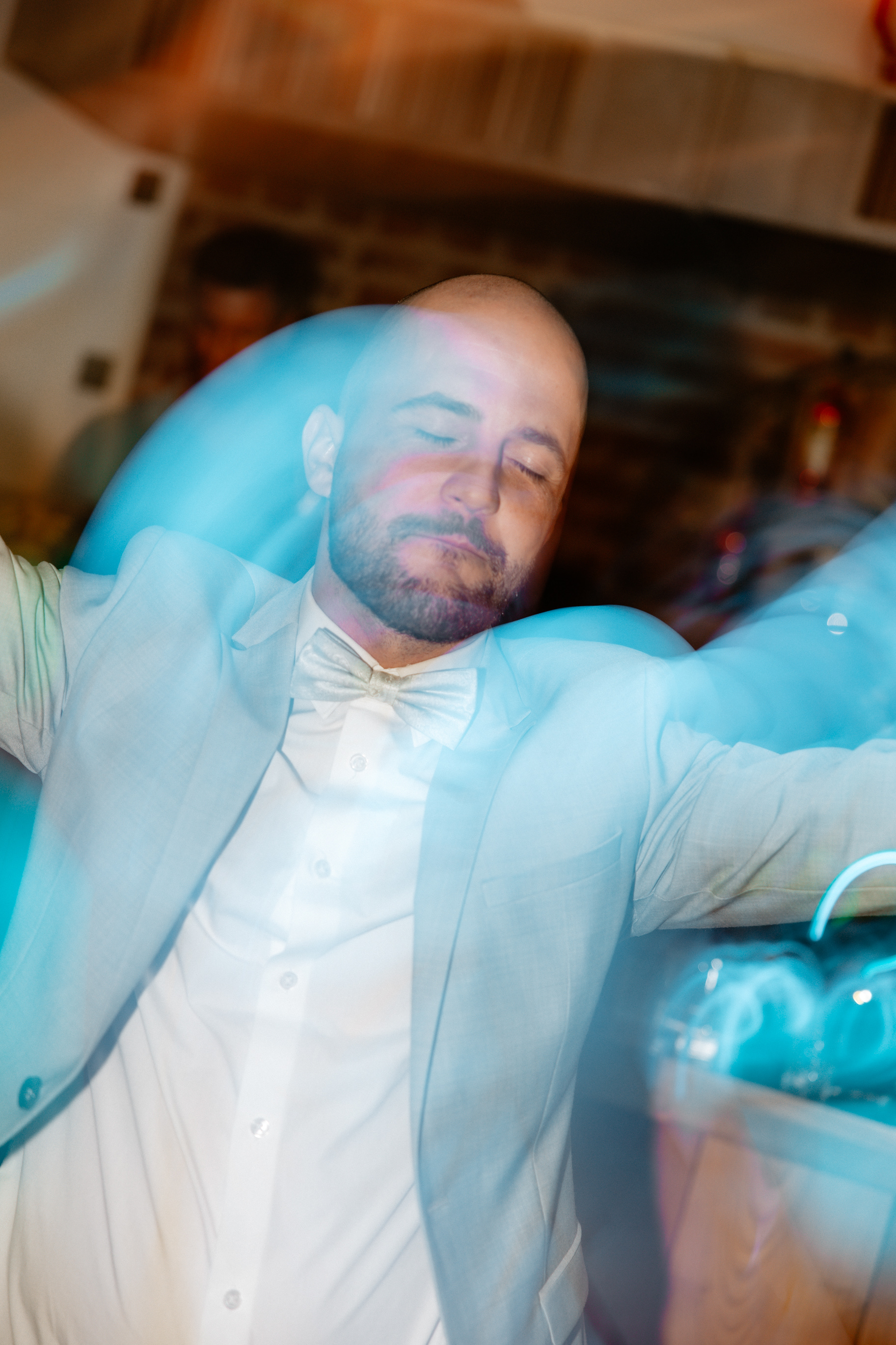 Ein Hochzeitsgast in einem hellen Anzug tanzt ausgelassen mit geschlossenen Augen, umgeben von blauen Lichtreflexionen