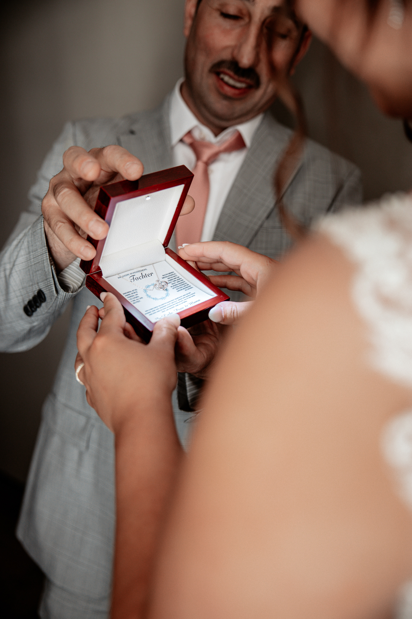Emotionaler Moment zwischen Braut Denise und ihrem Vater. Der Vater überreicht ihr eine Schmuckschatulle mit einer liebevollen Botschaft für seine Tochter. Die Braut nimmt das Geschenk mit gerührter Geste entgegen, während ihr Vater sie stolz und bewegt ansieht.