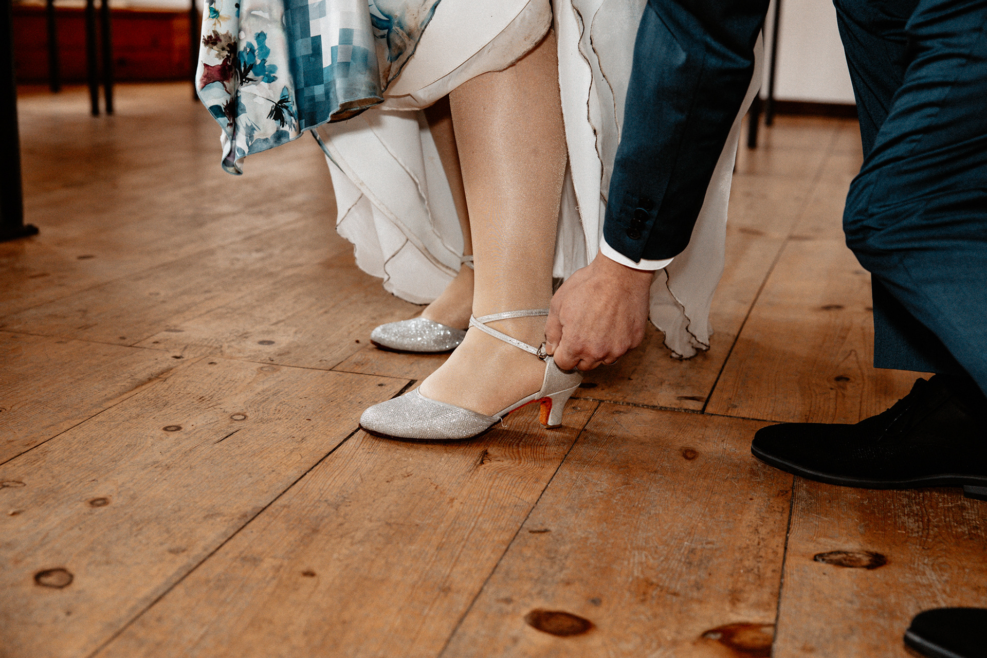 Romantischer Moment bei der Hochzeit von Claudia & Sven in der Goldberger Mühle, Mettmann: Der Bräutigam hilft der Braut beim Anziehen ihrer glitzernden Hochzeitsschuhe auf dem alten Holzboden des Standesamts. Hochzeitsfotograf Düsseldorf.