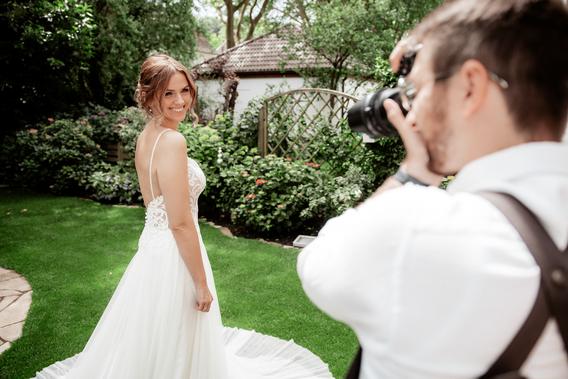 Christina Hochzeitsfoto beim Getting Ready. Die Braut strahlt in ihrem eleganten weißen Brautkleid, während der Hochzeitsfotograf sie im Garten fotografiert. Natürliche Hochzeitsfotografie in NRW.