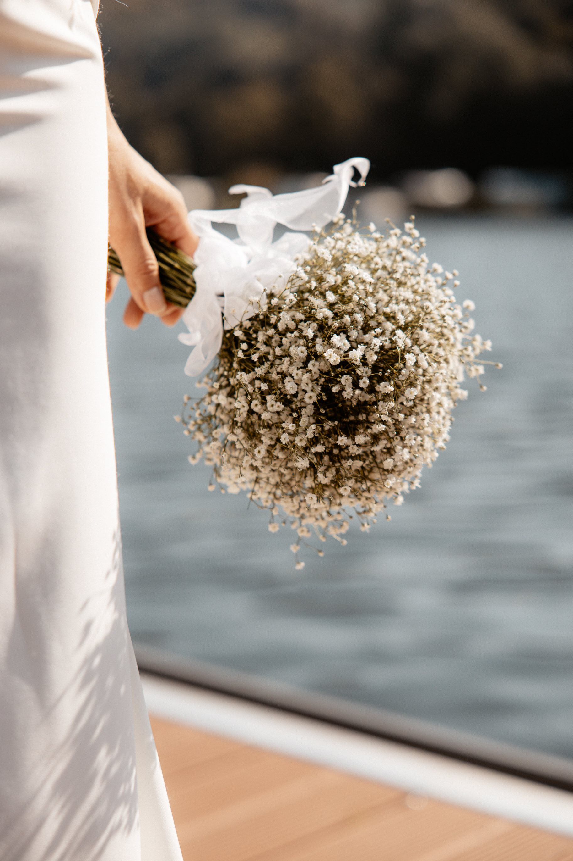 Detailaufnahme des Brautstraußes aus Schleierkraut, gehalten von Justine mit dem Wasser im Hintergrund.