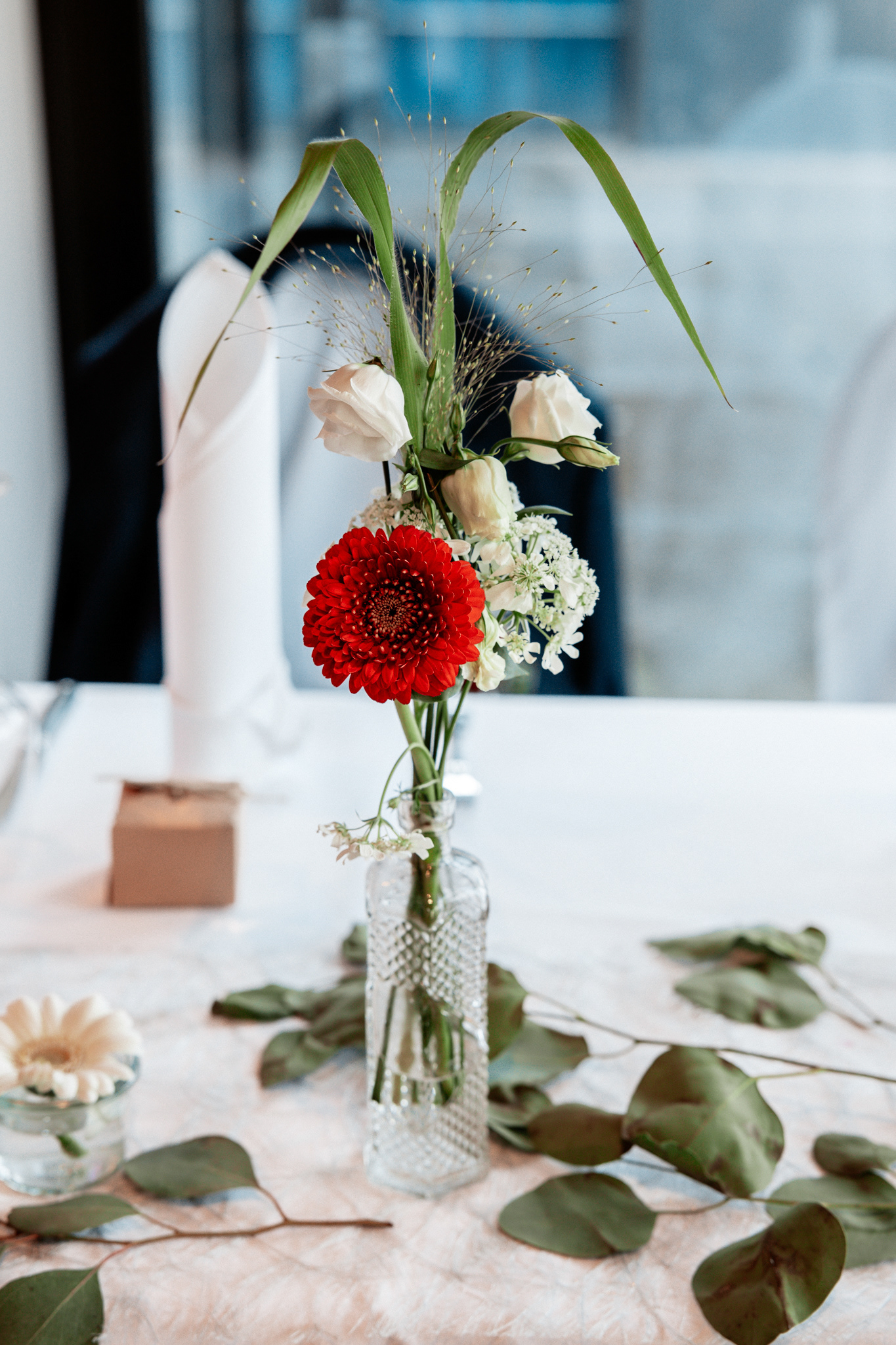 Detailaufnahme der Hochzeitstafel mit floraler Dekoration. Ein schlichter, aber eleganter Tischschmuck mit roten und weißen Blüten sowie grünen Blättern schmückt den festlichen Hochzeitstisch in Dortmund.