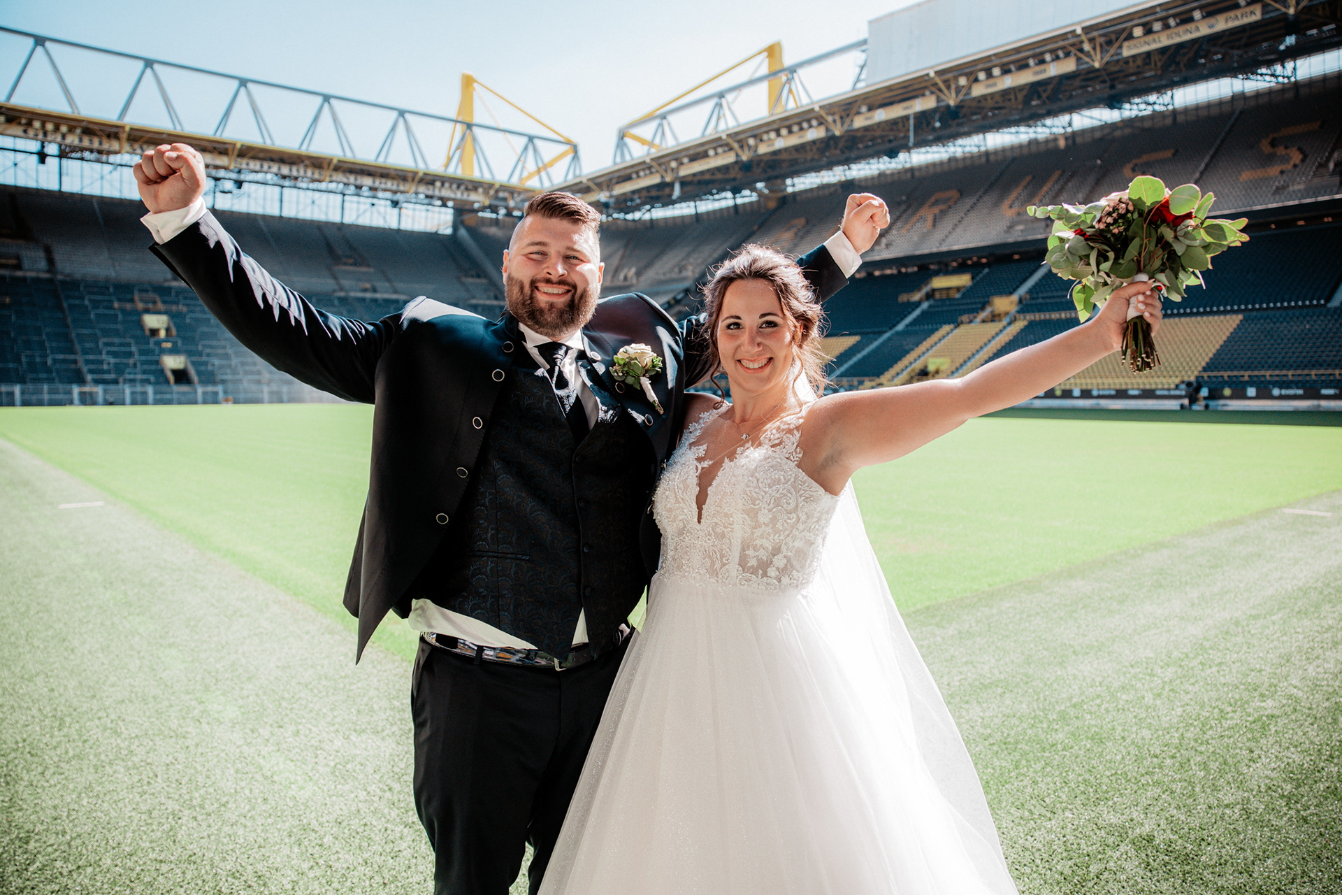 Denise und Michael stehen auf dem Spielfeld des Signal Iduna Parks und reißen die Arme in die Luft – ein emotionaler Höhepunkt der Hochzeit.