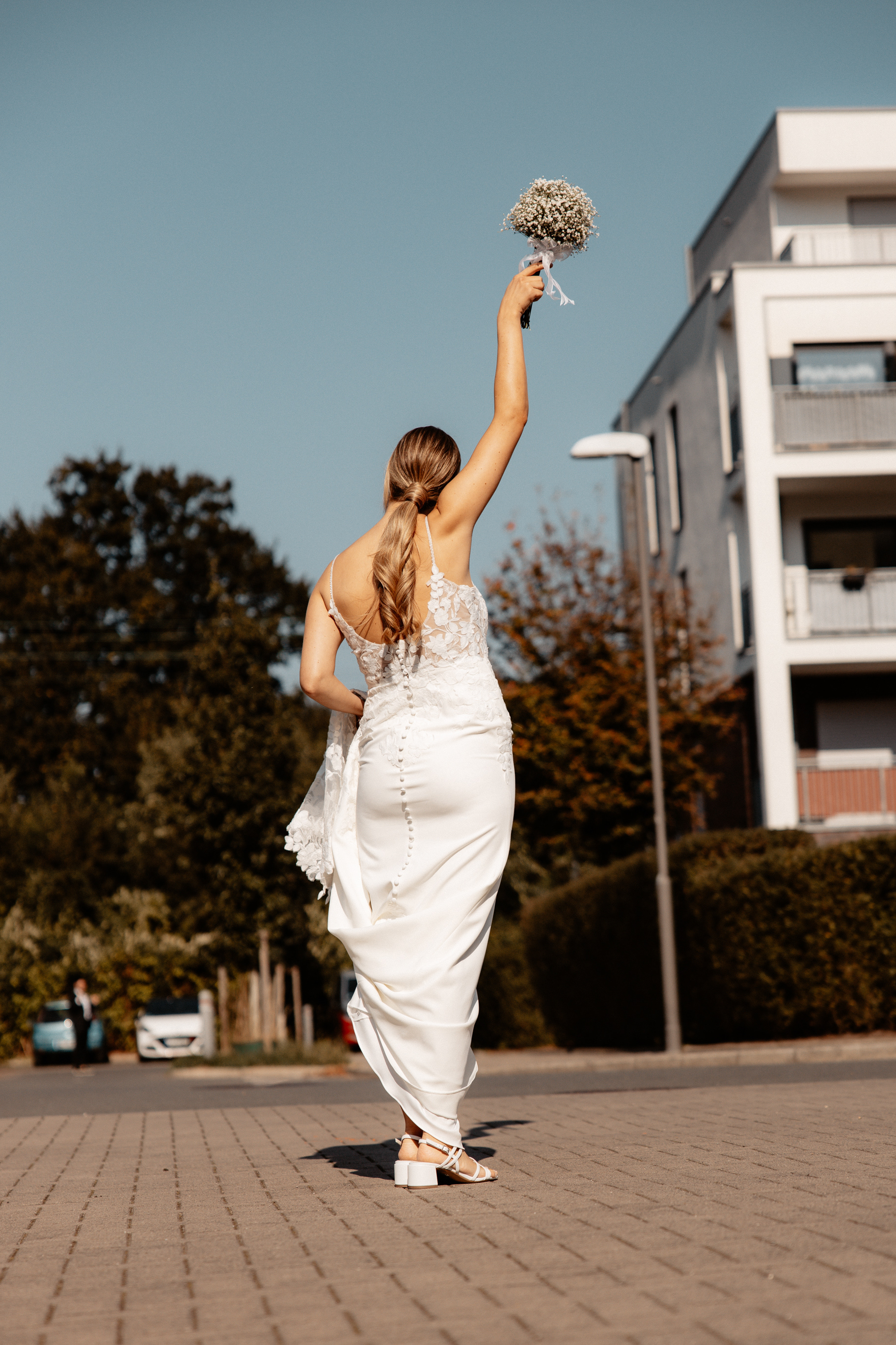 Die Braut hebt ihren Brautstrauß in die Luft, während sie selbstbewusst in die Ferne schreitet – ein Symbol für einen neuen Lebensabschnitt.