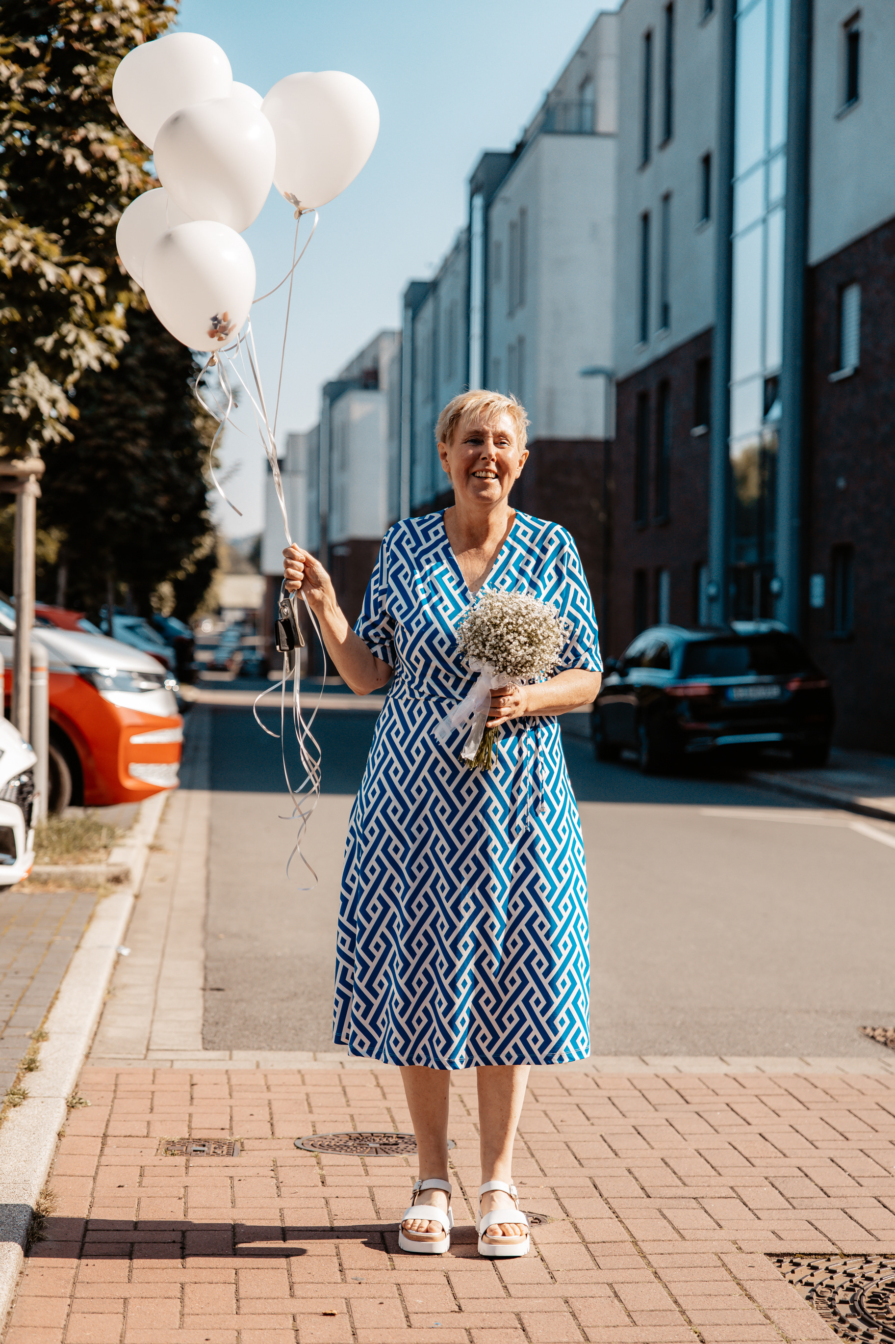 Die Mutter des Bräutigams hält weiße Luftballons und einen Blumenstrauß in den Händen, bereit für eine Überraschung für das Brautpaar. hält weiße Luftballons und einen Blumenstrauß in den Händen, bereit für eine Überraschung für das Brautpaar.