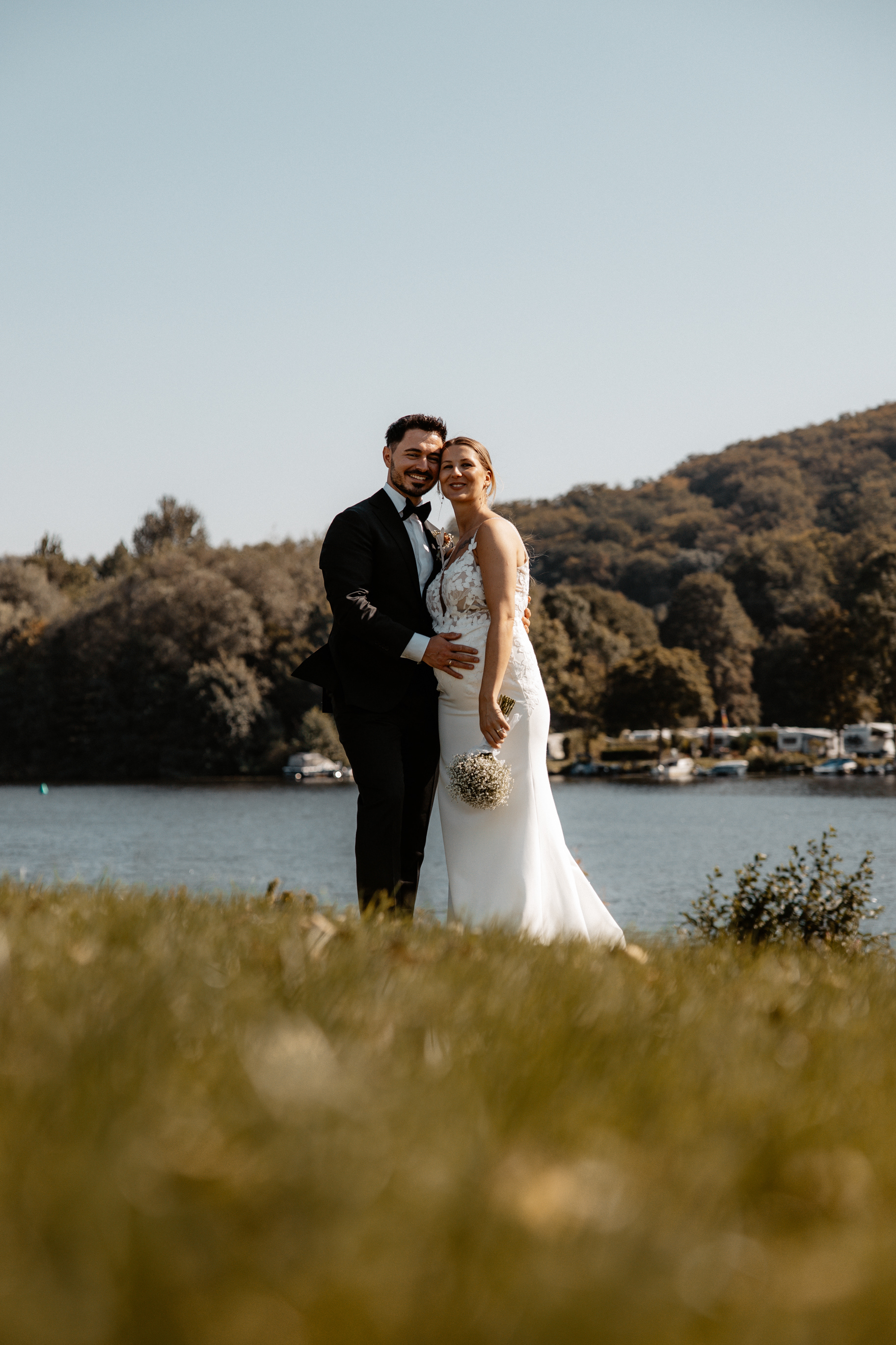 Das Brautpaar teilt einen liebevollen Moment bei Sonnenuntergang, während sie sich aneinander lehnen.