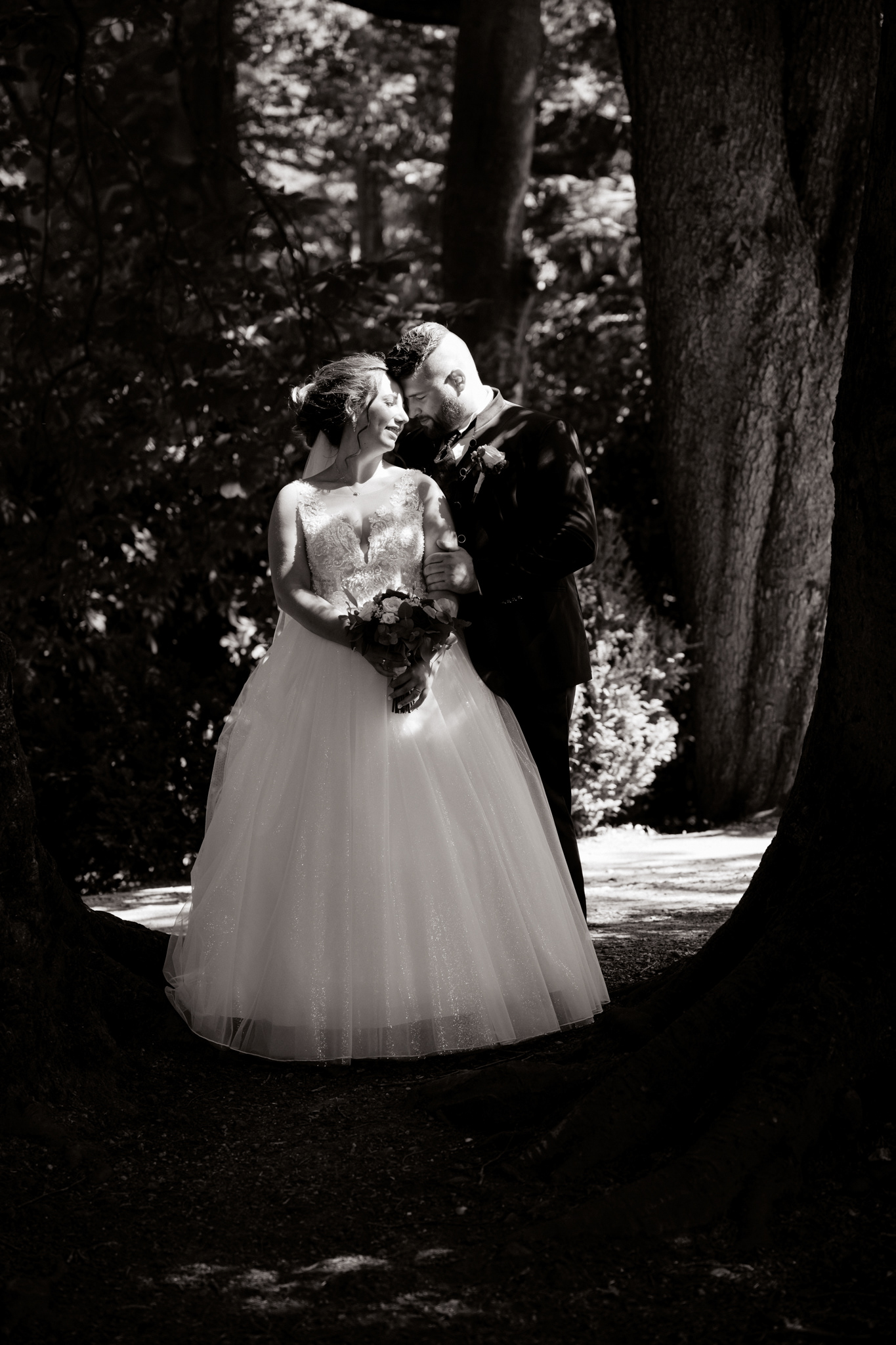 Ein klassisches Schwarz-Weiß-Porträt des Brautpaares inmitten alter Bäume, zeitlose Hochzeitsfotografie.
