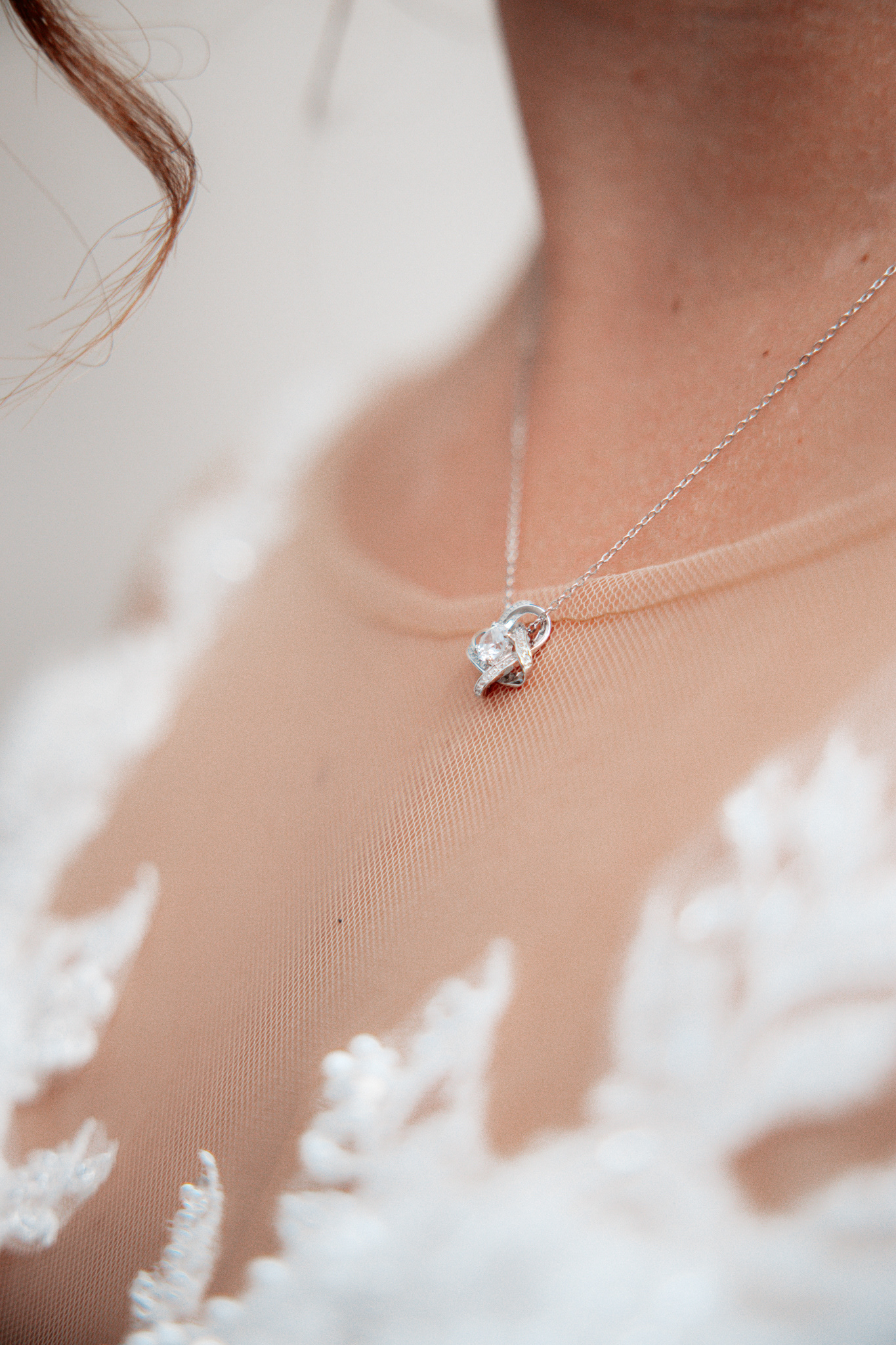 Detailaufnahme der filigranen Silberkette der Braut Denise. Das Schmuckstück mit funkelndem Anhänger ruht auf dem eleganten, mit Spitze verzierten Hochzeitskleid und fängt das Licht sanft ein.