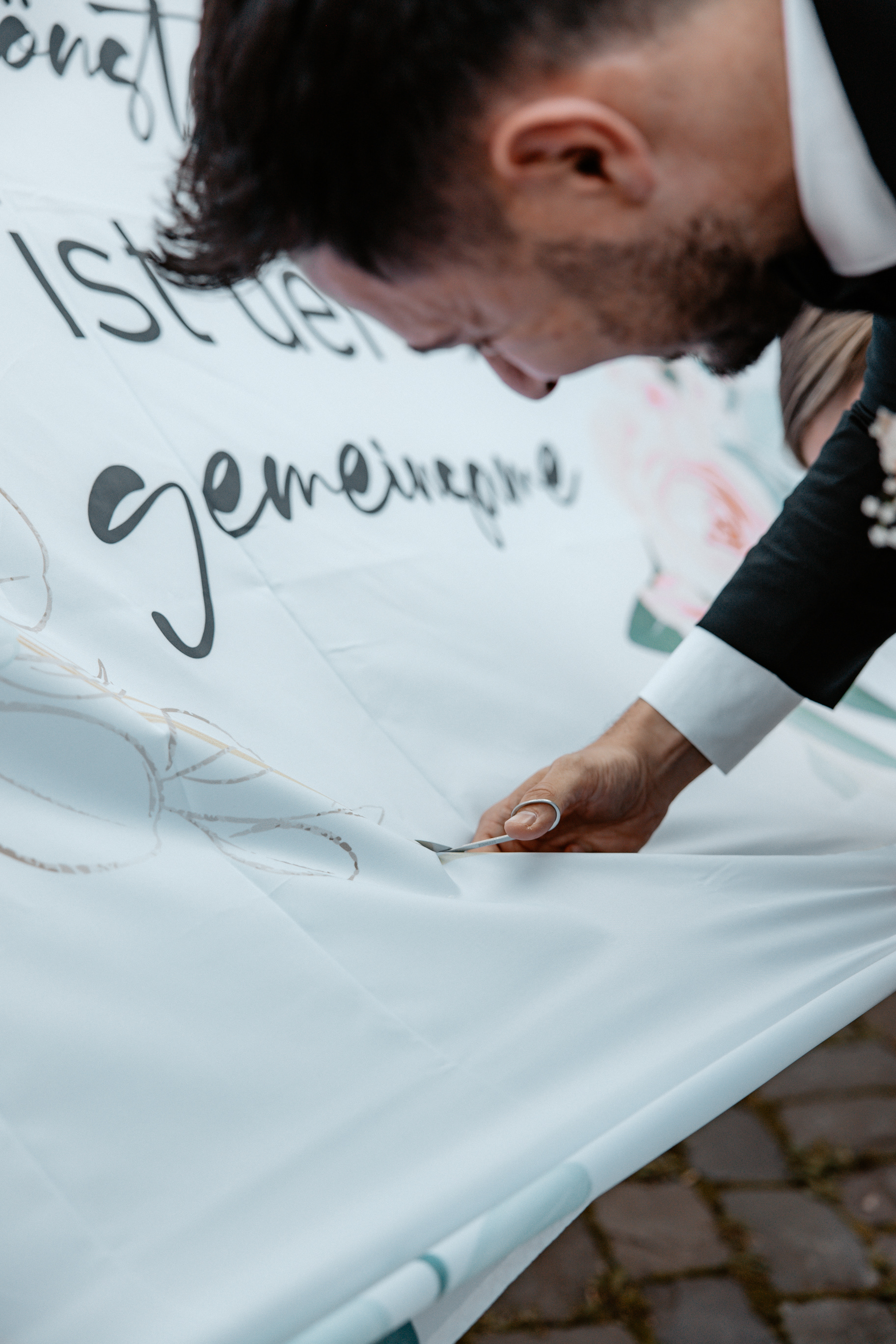 Der Bräutigam schneidet konzentriert ein Herz aus einem bedruckten Hochzeitstuch, als Teil einer traditionellen Hochzeitszeremonie.