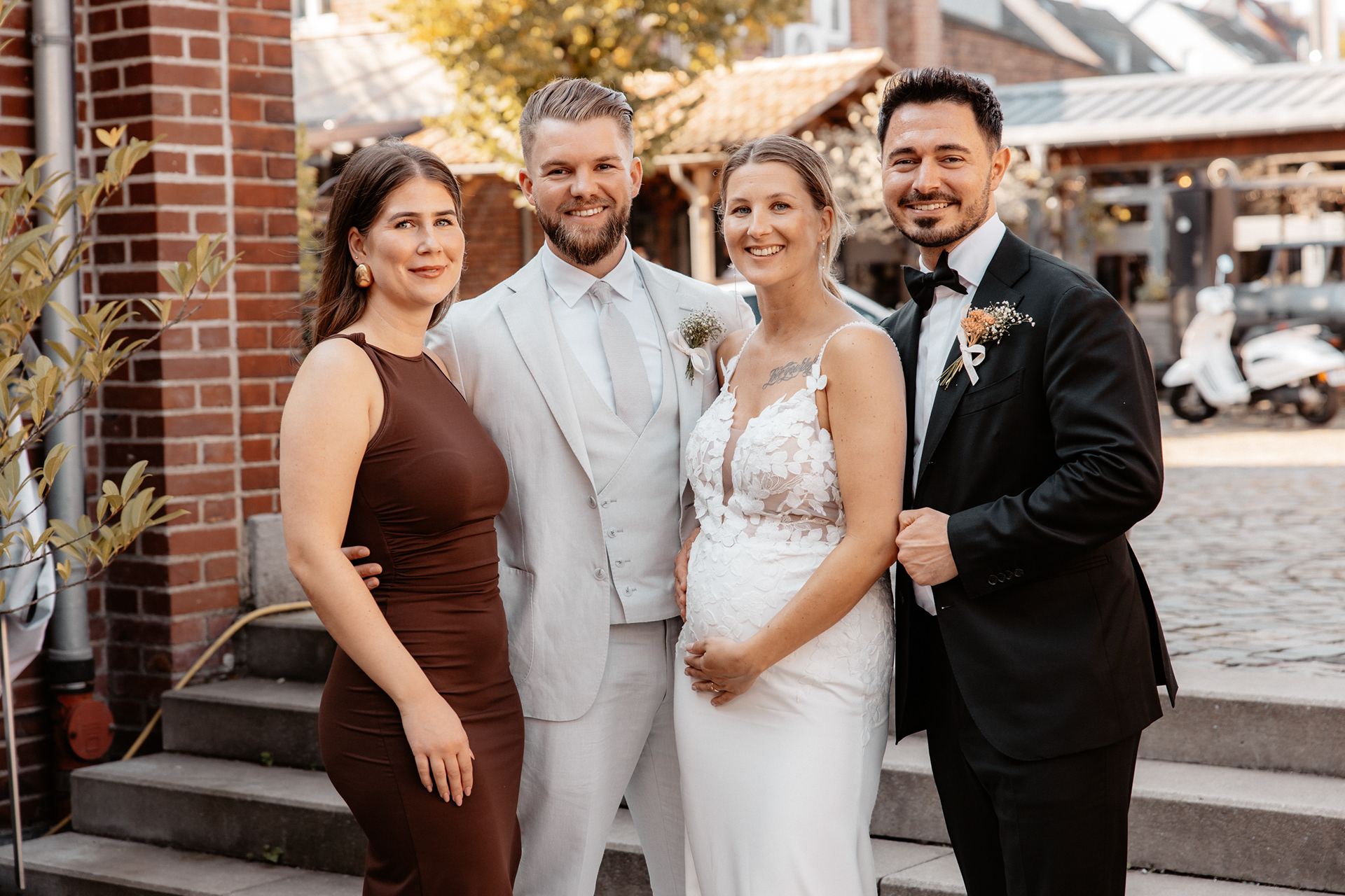Das Brautpaar posiert für ein Gruppenfoto mit zwei engen Freunden, beide Paare strahlen glücklich in die Kamera.