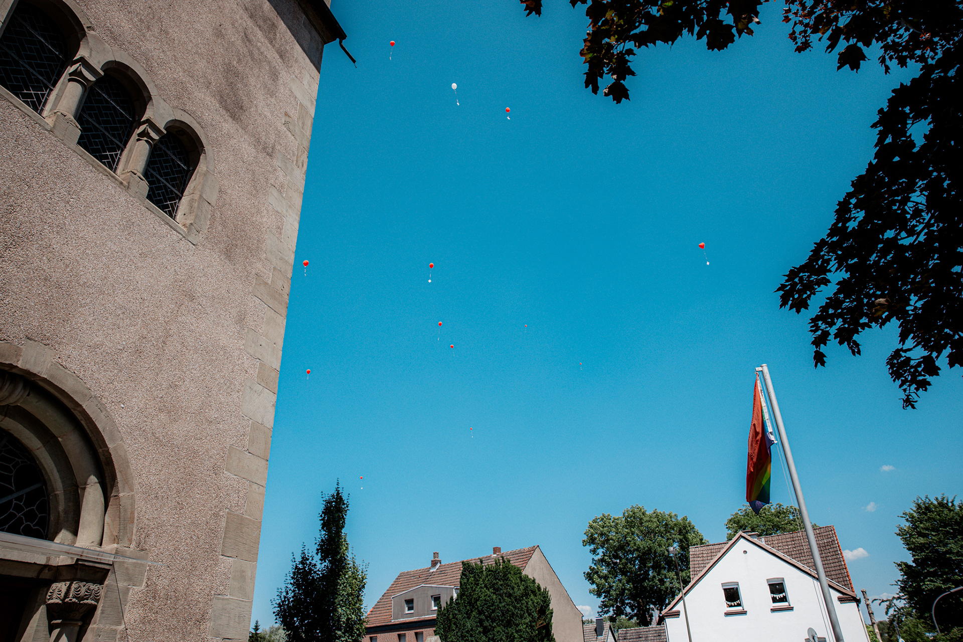 Rote und weiße Ballons steigen über der Kirche in den strahlend blauen Himmel. Ein symbolischer Moment der Wünsche und Glückwünsche für das frisch vermählte Paar.
