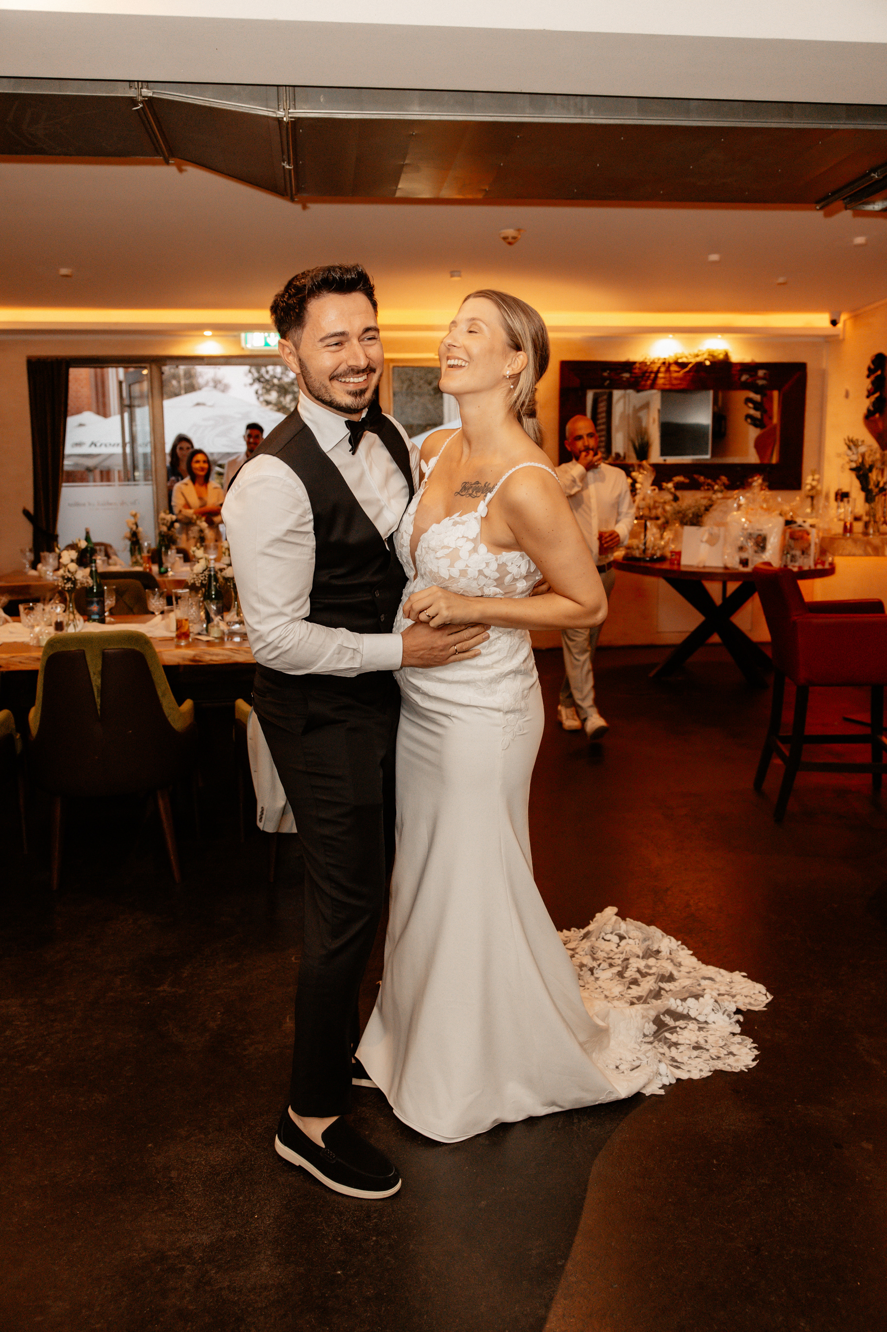 Das Brautpaar tanzt eng umschlungen und lachend auf der Tanzfläche der Hochzeitslocation, während Gäste im Hintergrund zuschauen.