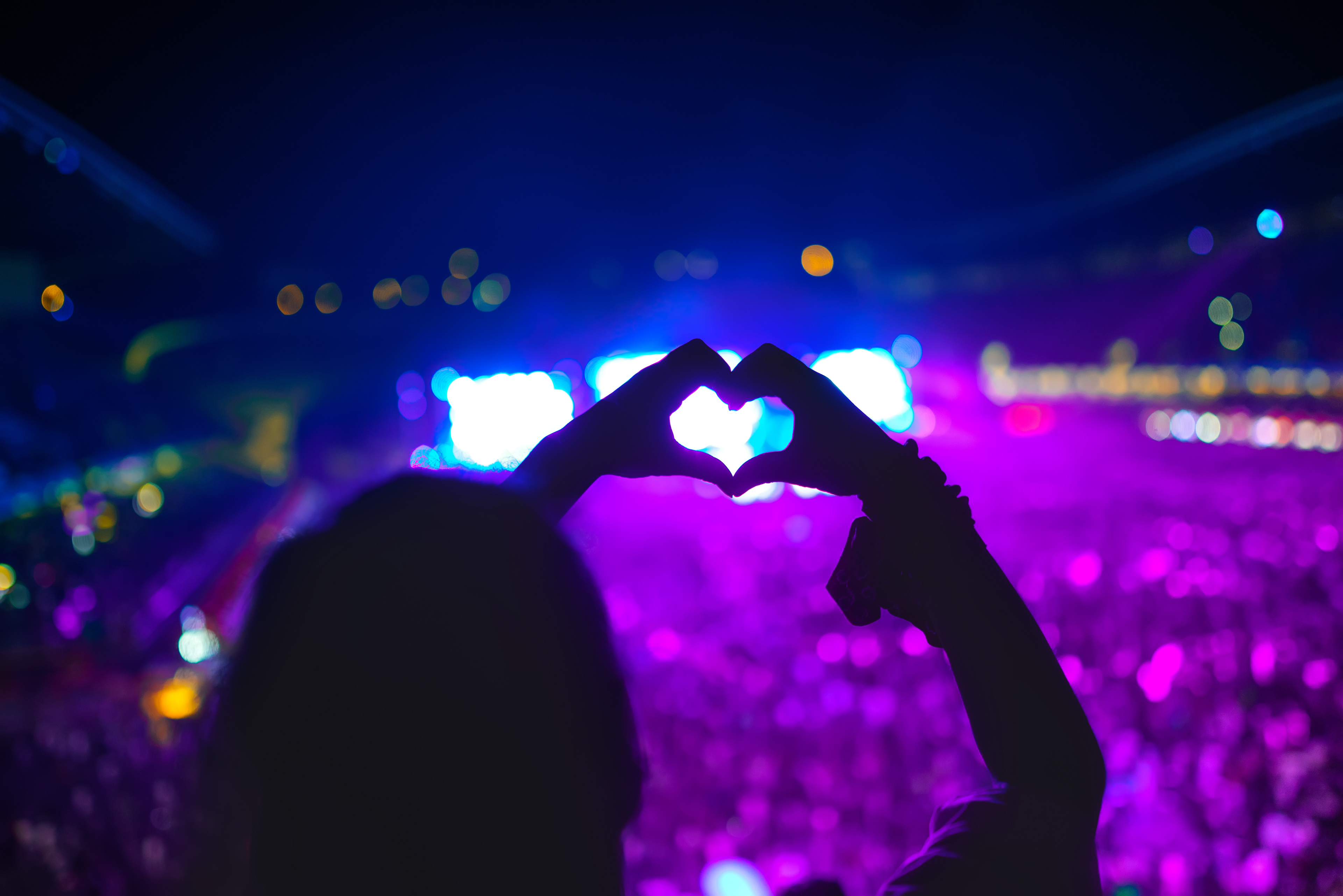 A silhouette of a person forming a heart shape with their hands at a concert, symbolizing the global love and connection fostered by Pan_Inc’s musical instruments.