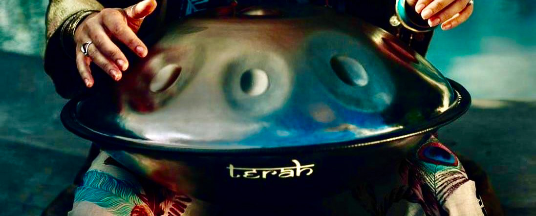 A musician’s hands gently rest on a Pan_Inc Stainless Series HandPan, showcasing intricate artwork on the instrument’s surface, reflecting a blend of musical excellence and visual creativity.