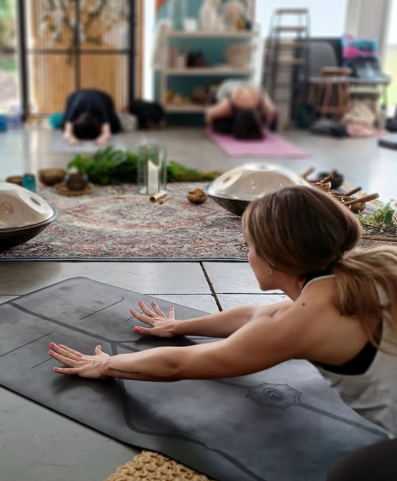 A tranquil yoga studio session with practitioners stretching on mats, accompanied by the soothing presence of Pan_Inc HandPans, enhancing the calm and meditative ambiance.