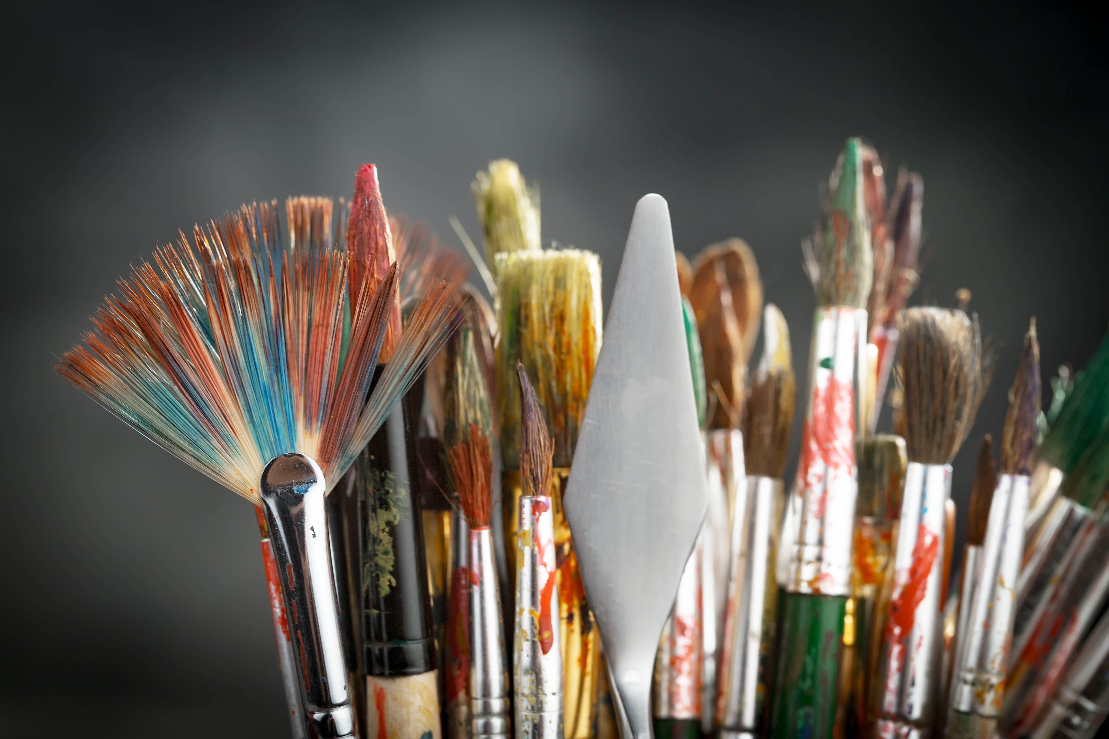 An array of paintbrushes with colorful bristles, splattered with a multitude of hues, indicative of the artistic customization Pan_Inc offers for their HandPans.