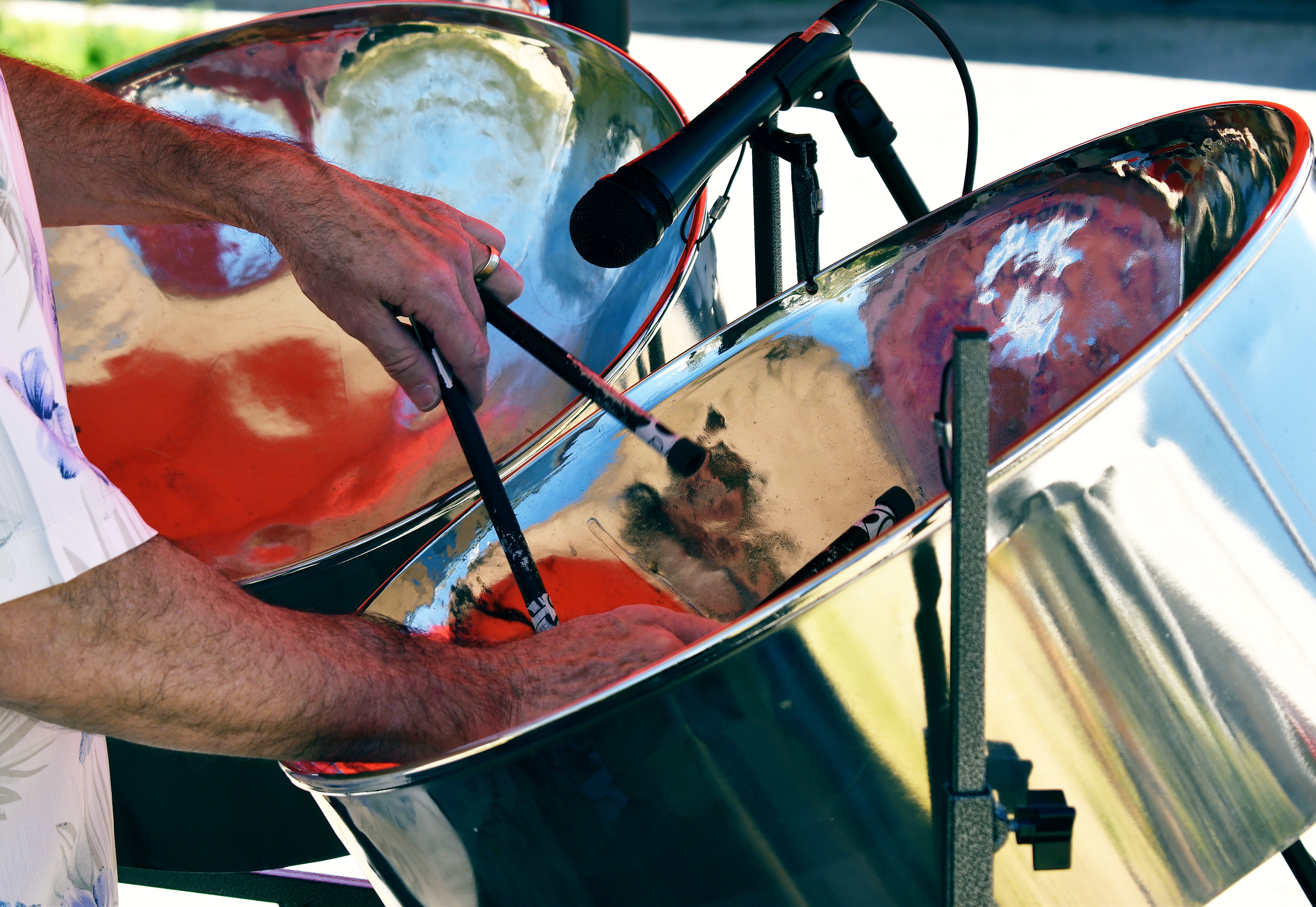 Close-up of a musician’s hands playing a steel pan drum with mallets, microphones set up for amplification, reflecting vibrant colors and the energy of a live performance.