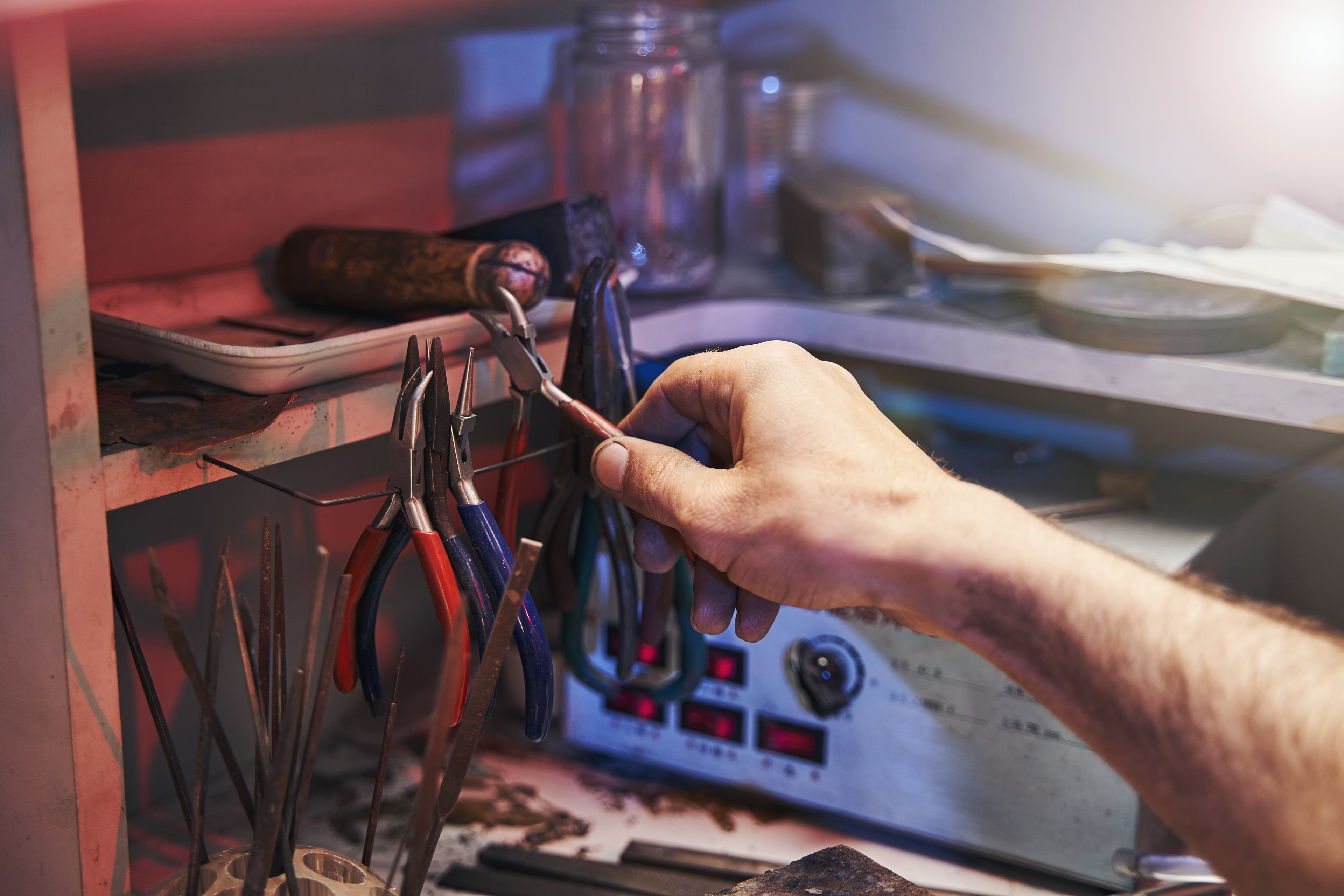 A craftsman’s hand holds a tuning tool over a workbench, surrounded by an assortment of specialized instruments, capturing the essence of Pan_Inc’s commitment to creating perfectly tuned HandPans.