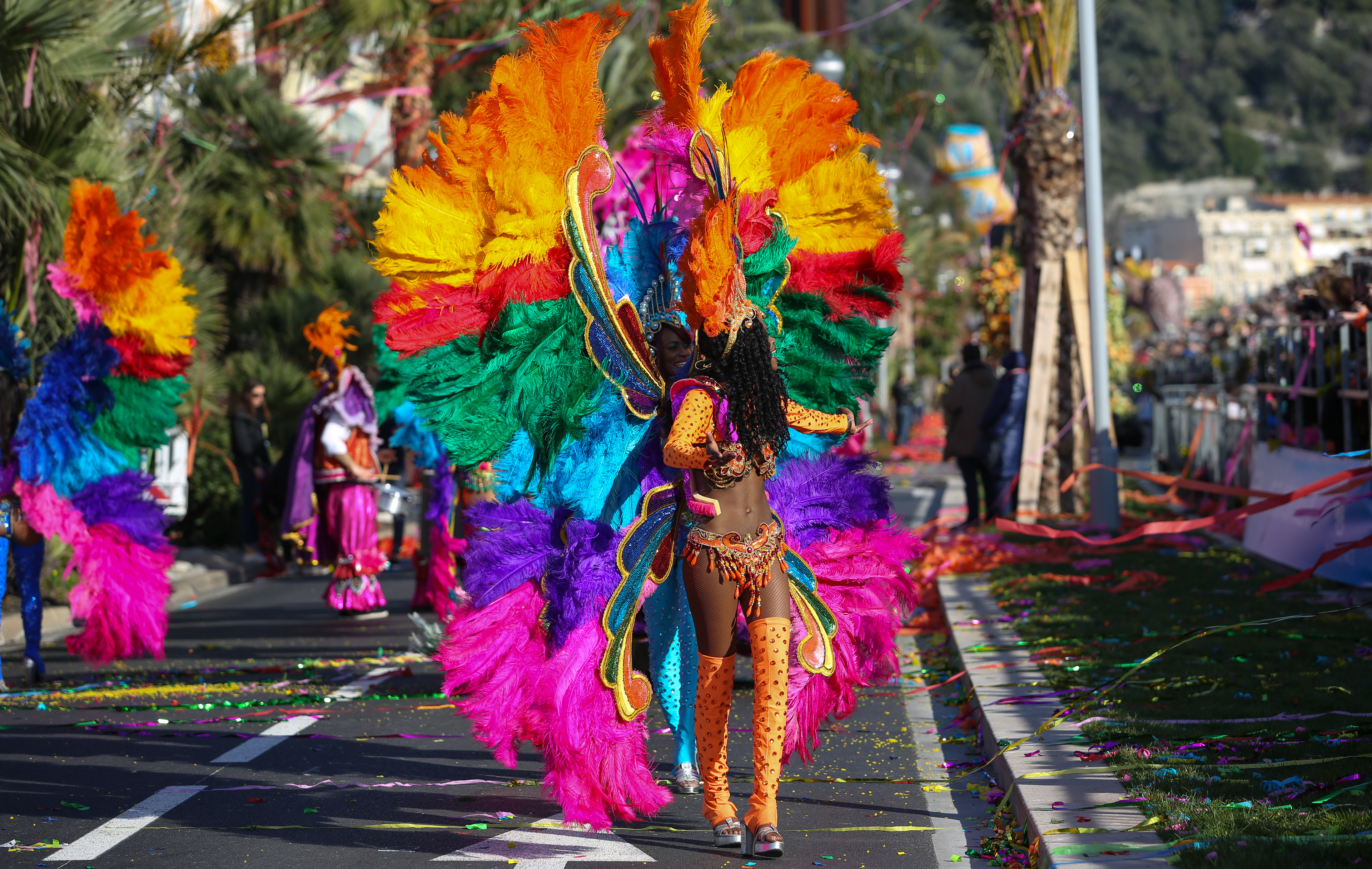 A carnival performer adorned in a magnificent costume with rainbow feathers moves through the streets, echoing the festive spirit of Trinidad’s carnival, an inspiration for Pan_Inc’s vibrant musical creations.