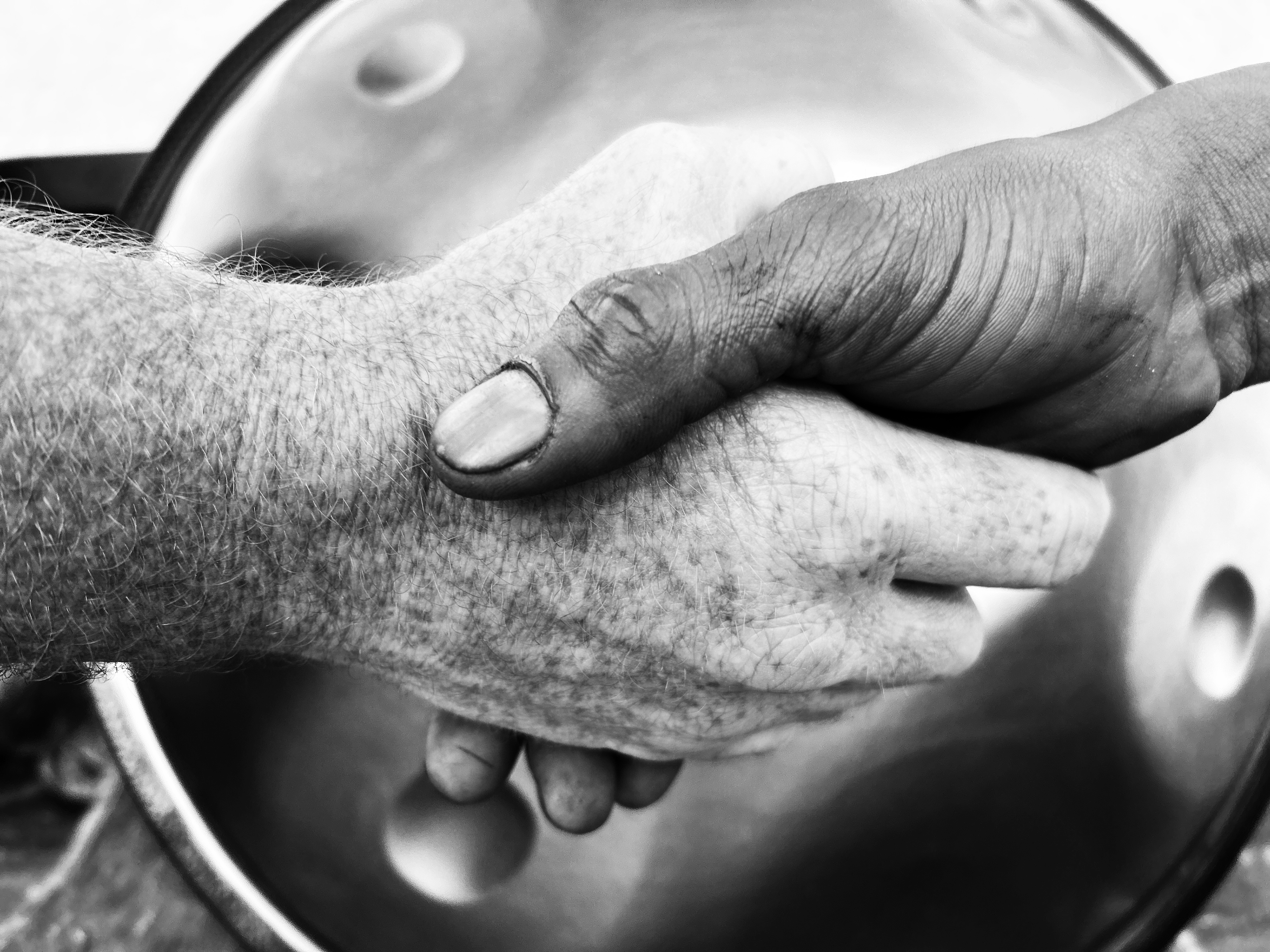 Close-up black and white photo of two hands shaking over a HandPan drum, symbolizing trust, craftsmanship, and personal service by Pan_Inc.